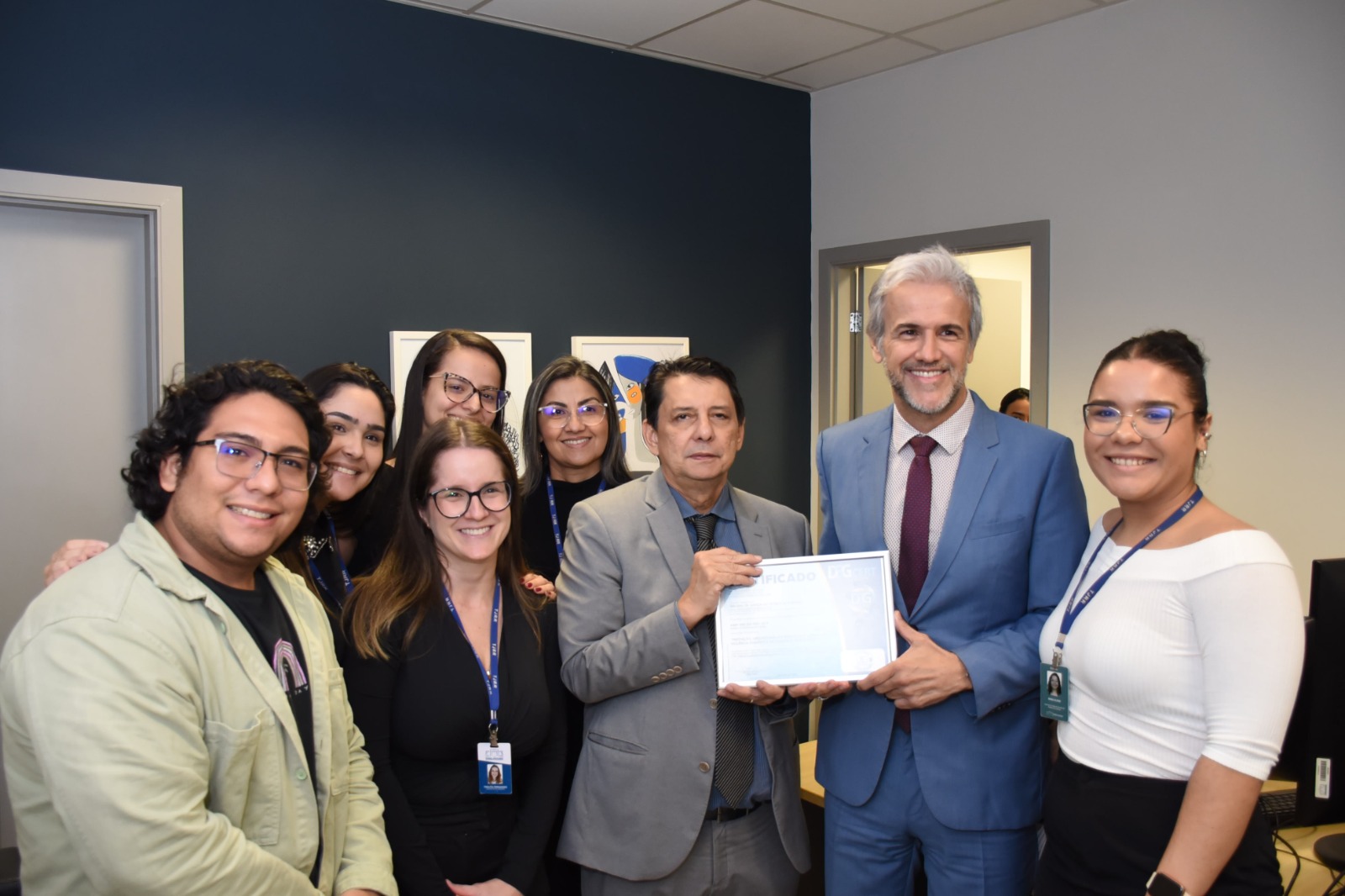 Foto colorida mostra oito pessoas posando para a foto. Ao centro, o desembargador Jésus Nascimento e o juiz Jaime Plá, ambos segurando a certificação