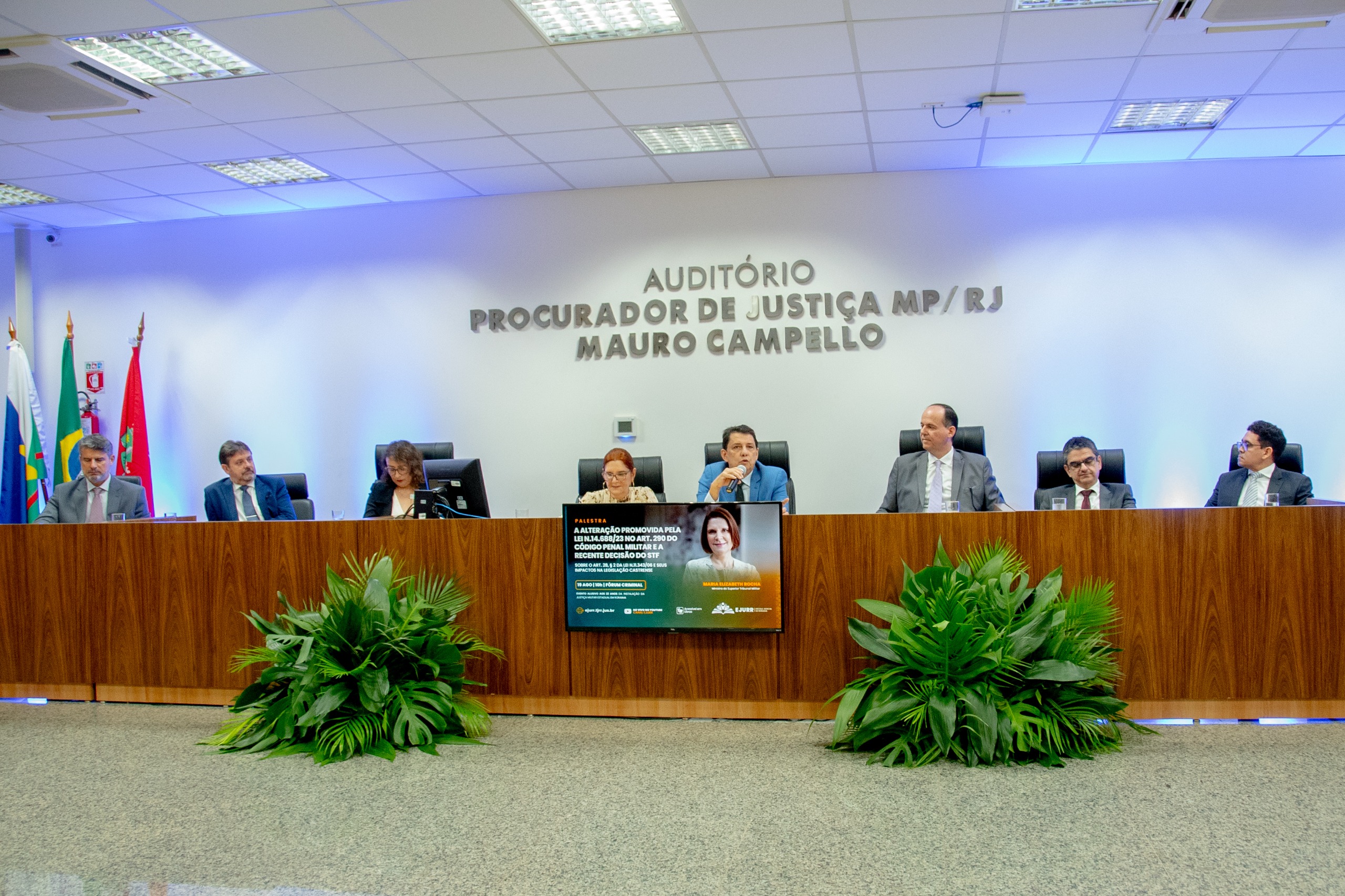 foto colorida mostra a mesa de autoridades com a ministra do Superior Tribunal Militar (STM), Maria Elizabeth Rocha, o vice-presidente do TJRR, desembargador Ricardo Oliveira; o diretor da Ejurr, desembargador Cristóvão Suter; o juiz convocado Luiz Fernando Mallet; o procurador-geral de Justiça, Fábio Stica; a juíza titular da 1ª Vara do Júri e da Justiça Militar, Lana Leitão; e o juiz titular da 2ª Vara do Júri e da Justiça Militar, Breno Coutinho, durante palestra no Fórum Criminal Ministro Evandro Lins e Silva.