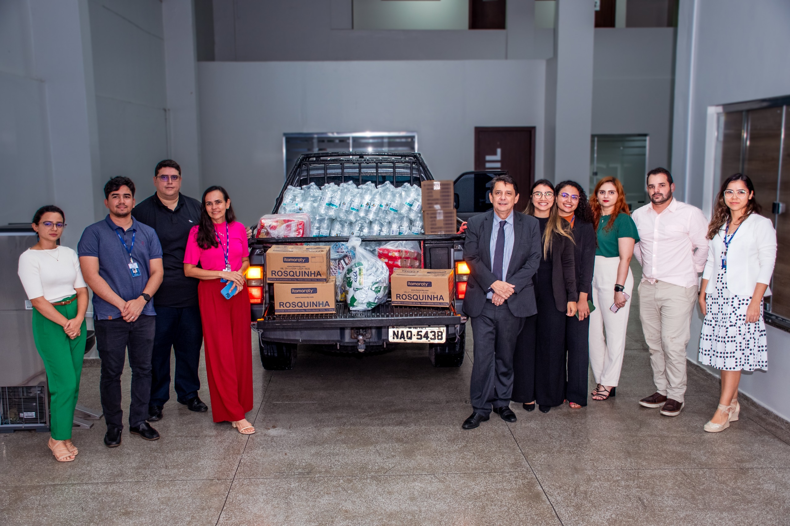 Foto colorida mostra 10 pessoas posando ao lado do carro cheio de doações