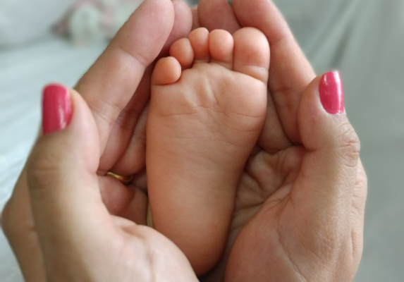 Na imagem contém uma mão segurando o pé de uma criança.