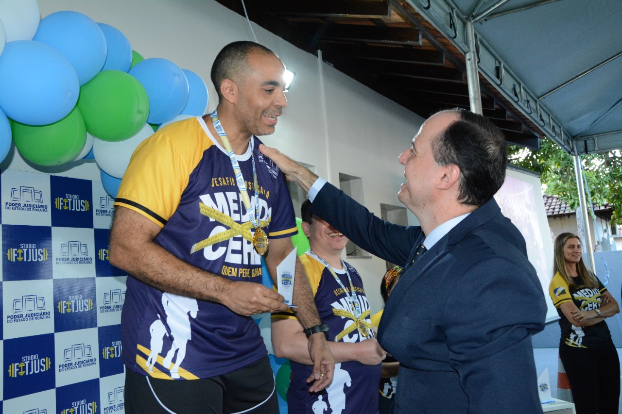 Foto colorida que contém o presidente do TJRR, desembargador Cristôvão Súter, colocando medalha em participante. 
