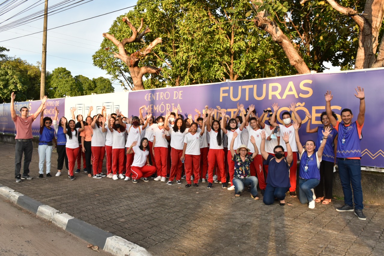 Imagem colorida contém alunos da Escola Estadual Oswaldo Cruz e servidores do TJRR, em frente ao banner do Centro de Memória do TJRR.