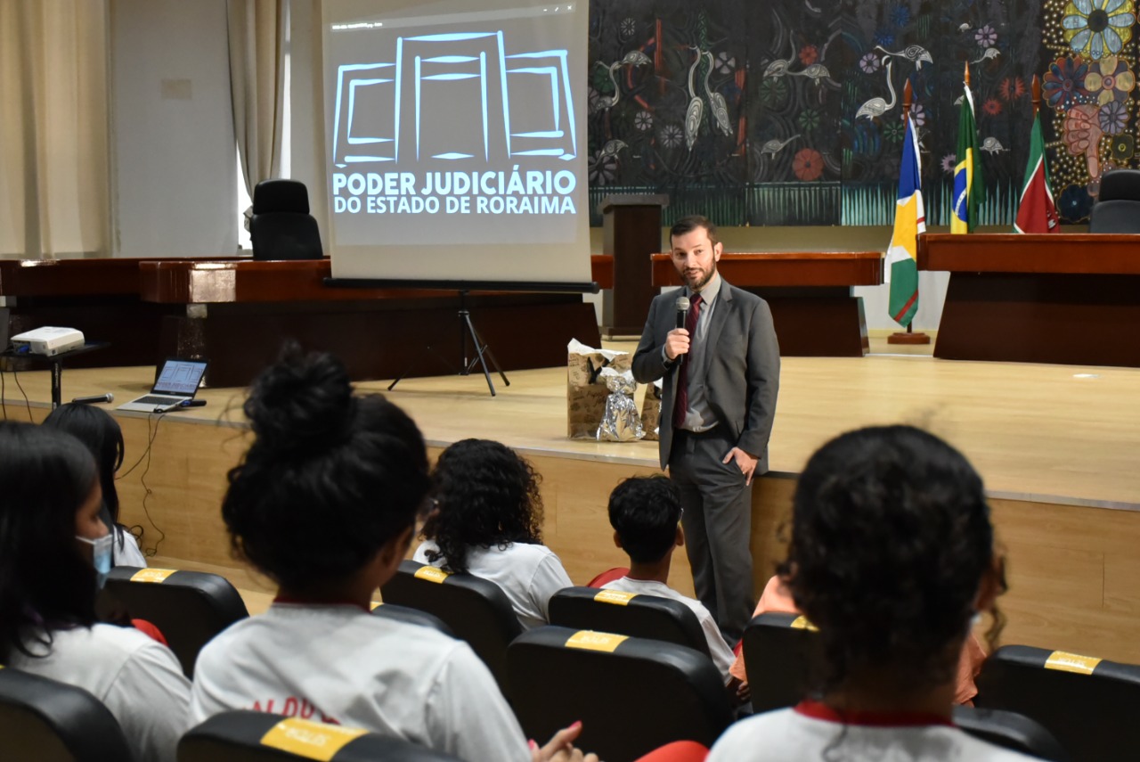 Imagem colorida contém o Juiz auxiliar do TJRR, Dr Bruno Fernandes Alves Costa, palestrando para alunos da Escola Estadual Oswaldo Cruz, no Tribunal do Pleno do TJRR.