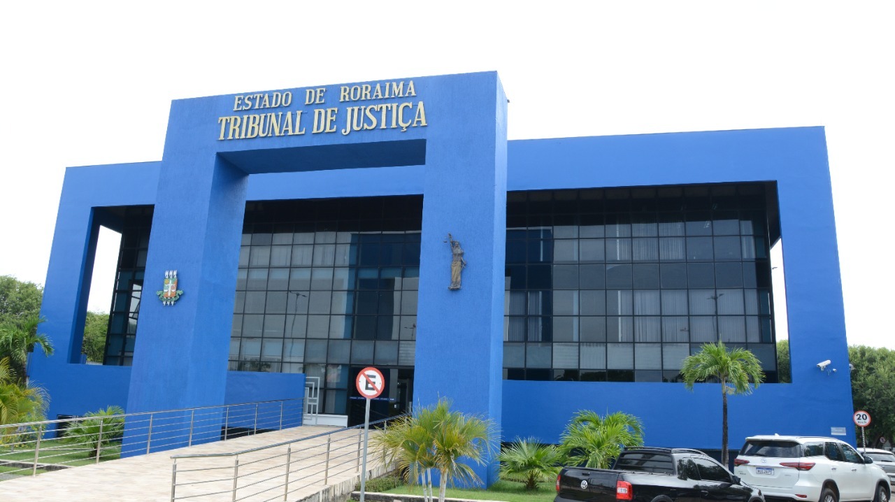 Imagem colorida mostra a fachada do prédio do Palácio da Justiça, o edifício pintado na cor azul escuro está identificado com o nome “ Estado de Roraima, Tribunal de Justiça” pintado de dourado.