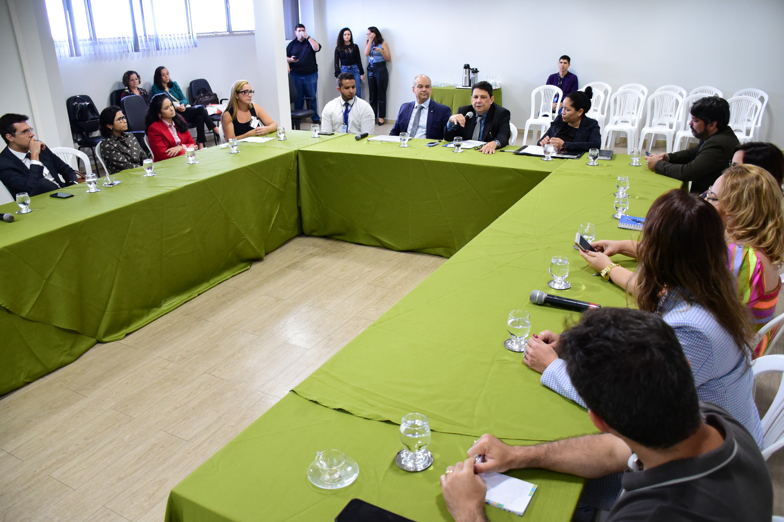 foto colorida mostra o presidente do TJRR, desembargador Jésus Nascimento, falando ao microfone aos membros do Comitê da Saúde. Todos estão sentados frente a uma mesa organizada em formato de U.