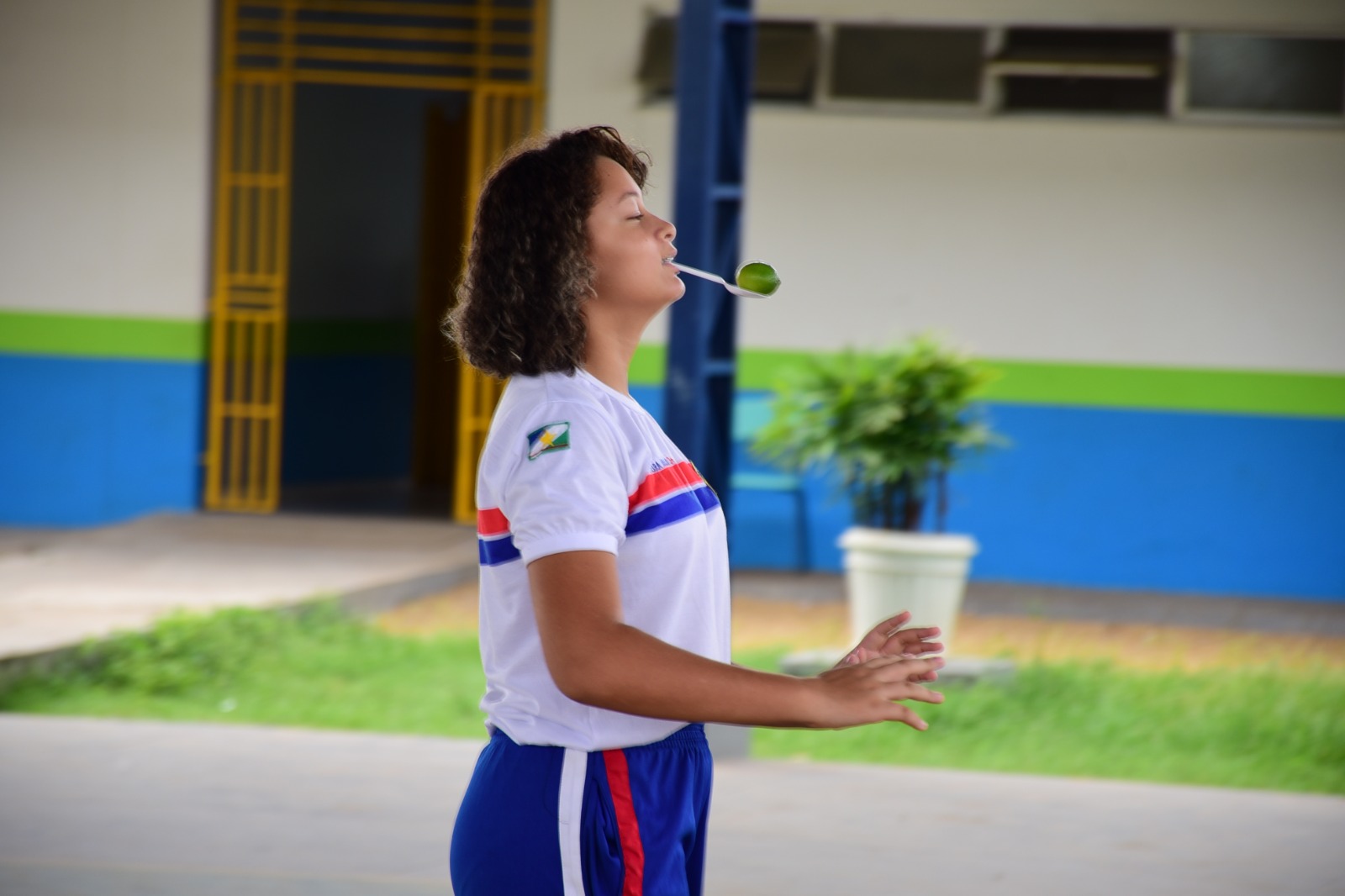 foto colorida de uma jovem fardada equilibrando uma colher na boca com um limão