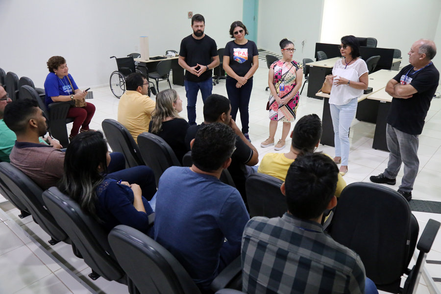 foto colorida na area interna de um auditoria que possuem gente sentada nas cadeiras e afrente há cinco colaboradores do TJRR falando ao microfone