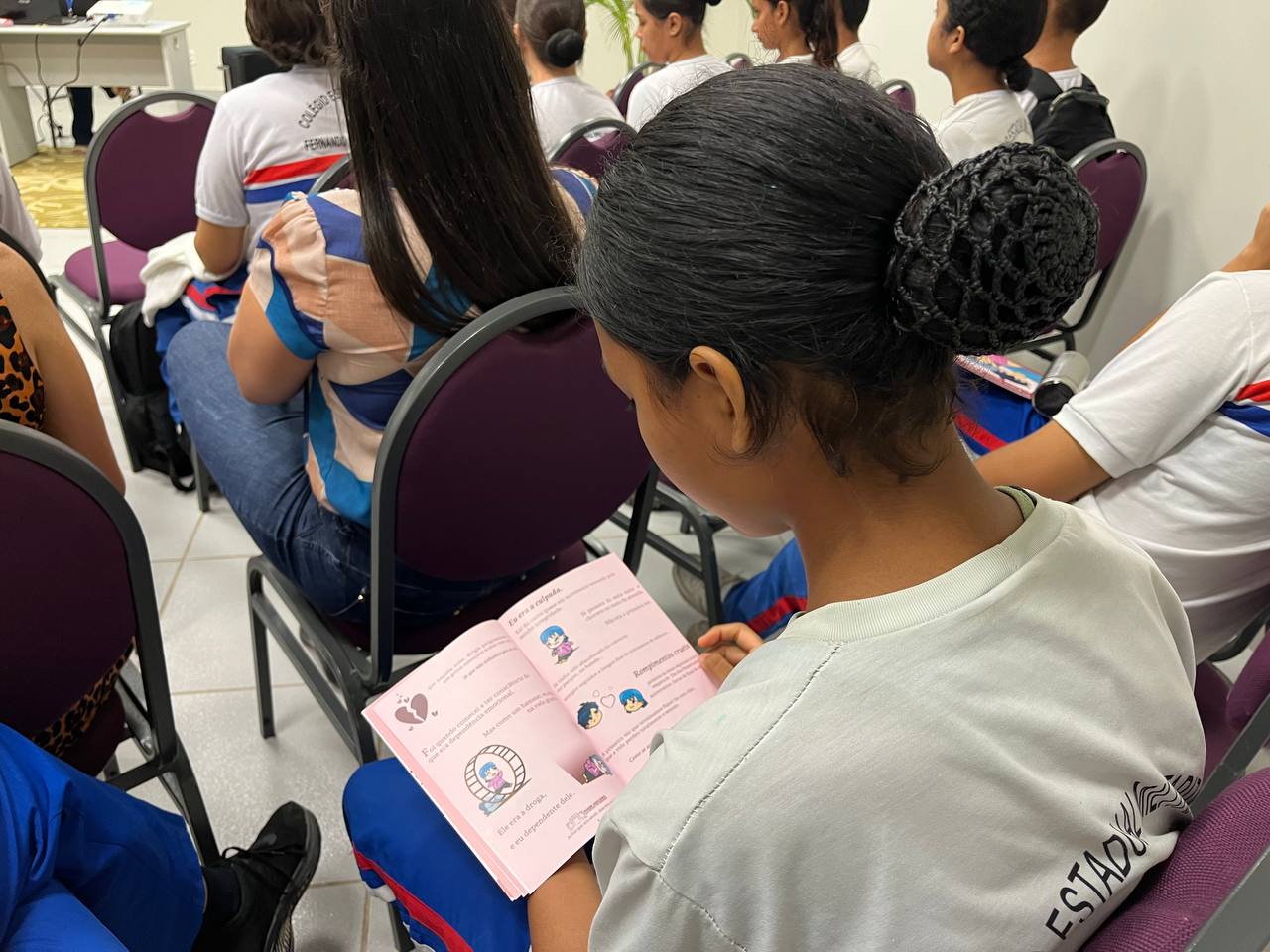  foto colorida tirada de uma aluna da escola militarizada lendo a cartilha entregue da CEVID
