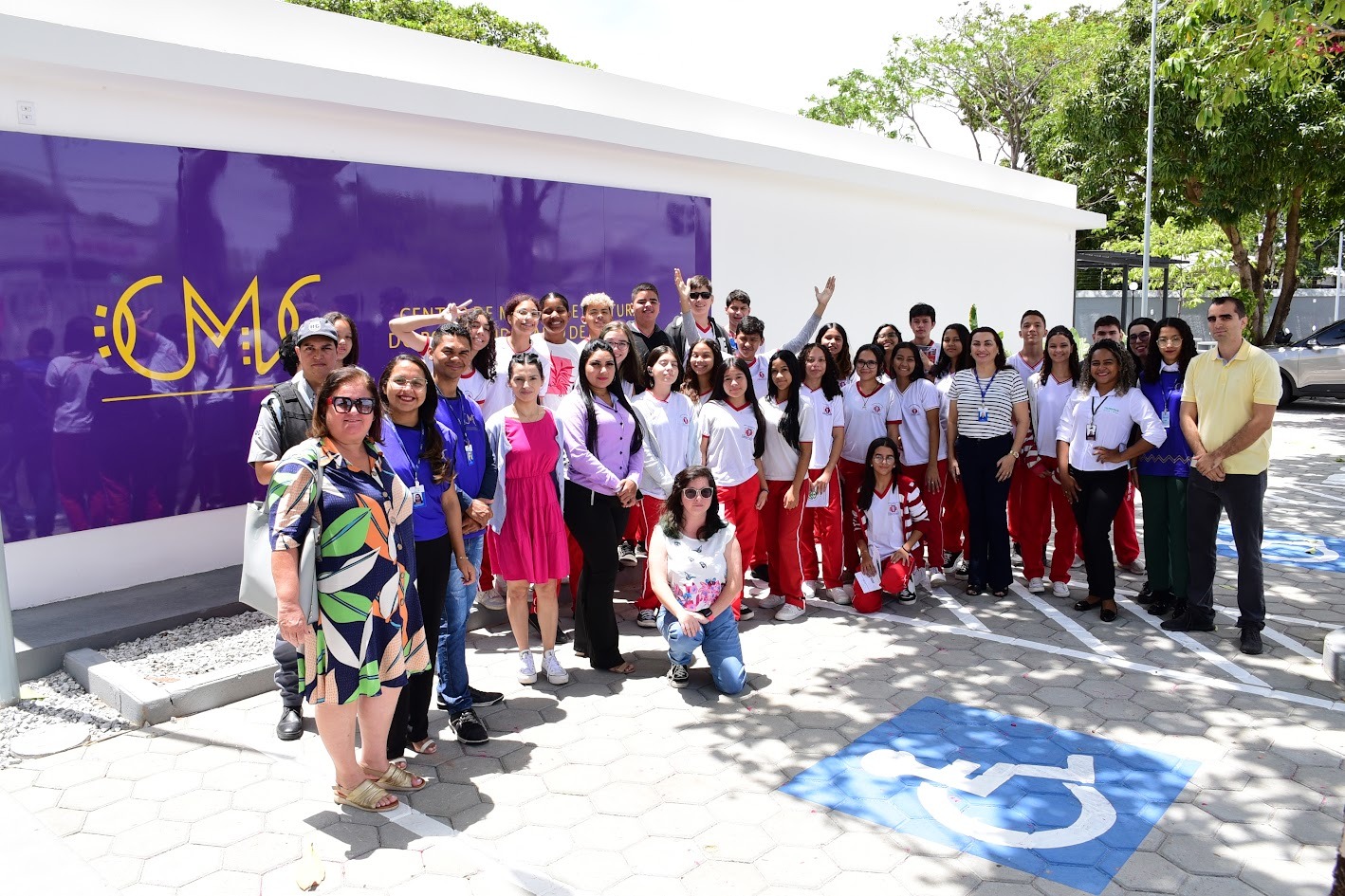 Foto colorida mostrando estudantes do ensino fundamental, juntamente com gestores e professores, além de servidores do Centro de Memória e Cultura, posando para foto em frente a fachada do prédio. 