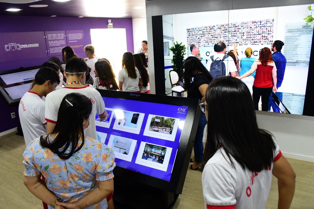 Foto colorida mostrando estudantes do ensino fundamental observando um dos totens interativos do Centro de Memória e Cultura. 