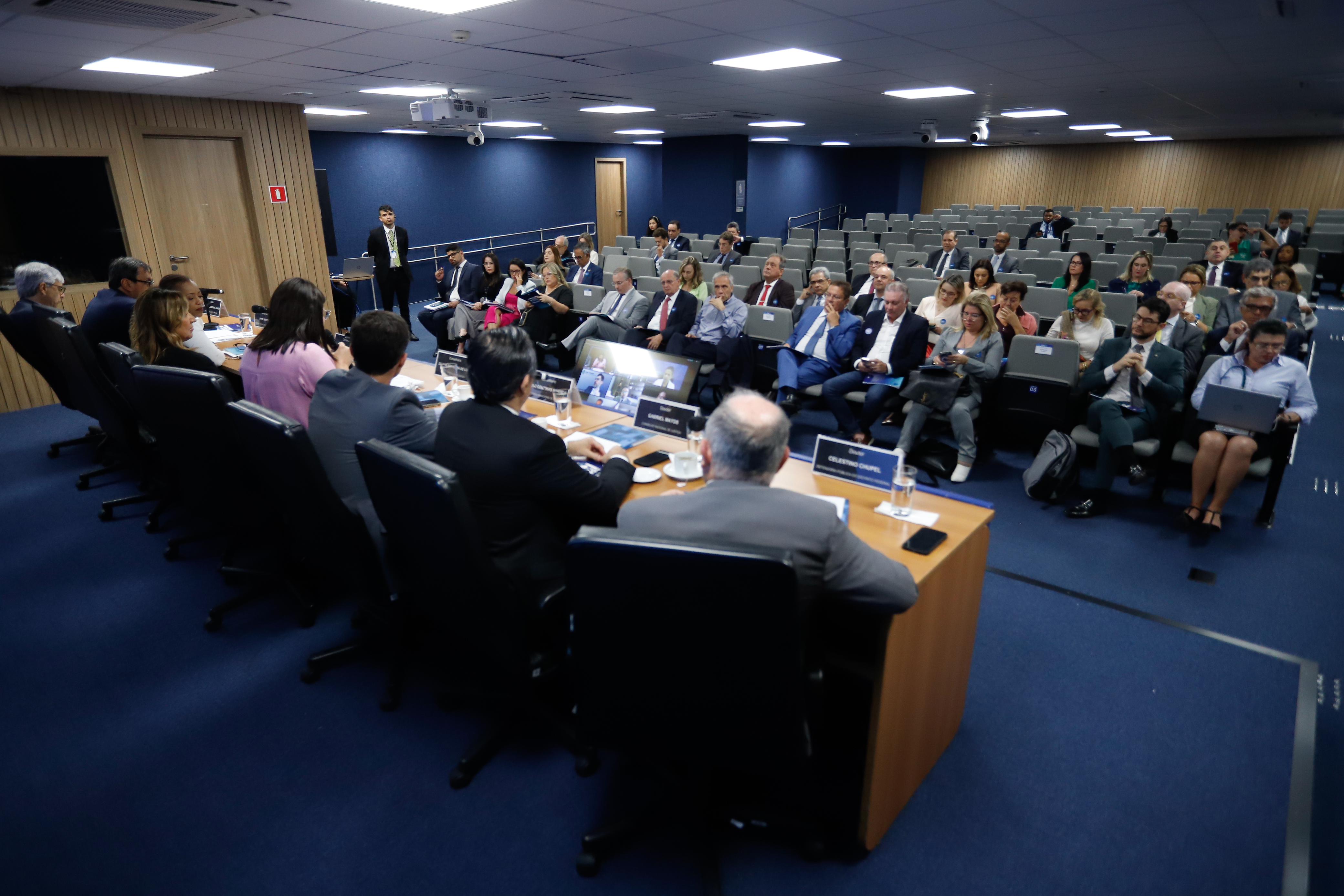 Foto colorida mostrando uma mesa de autoridade e um auditório 