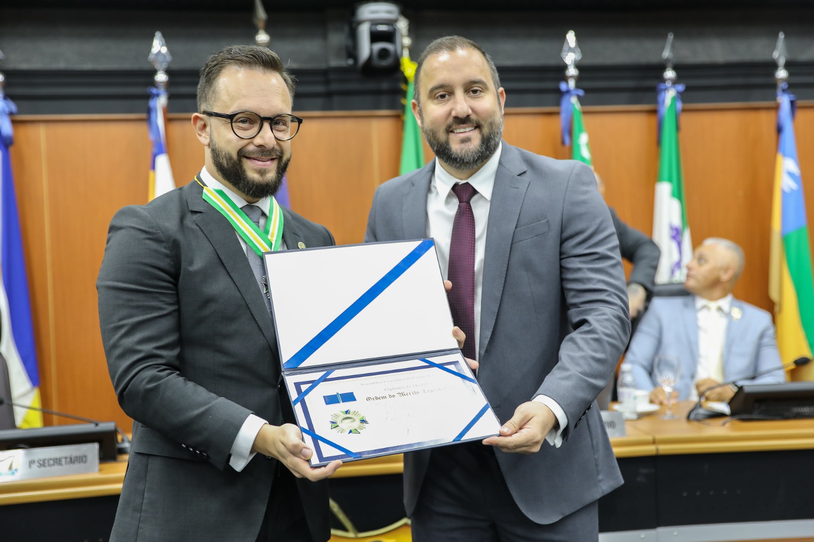 Foto colorida mostra o juiz auxiliar da presidência, Esdras Silva Benchimol posando para foto recebendo o certificado da Ordem do Mérito Legislativo.