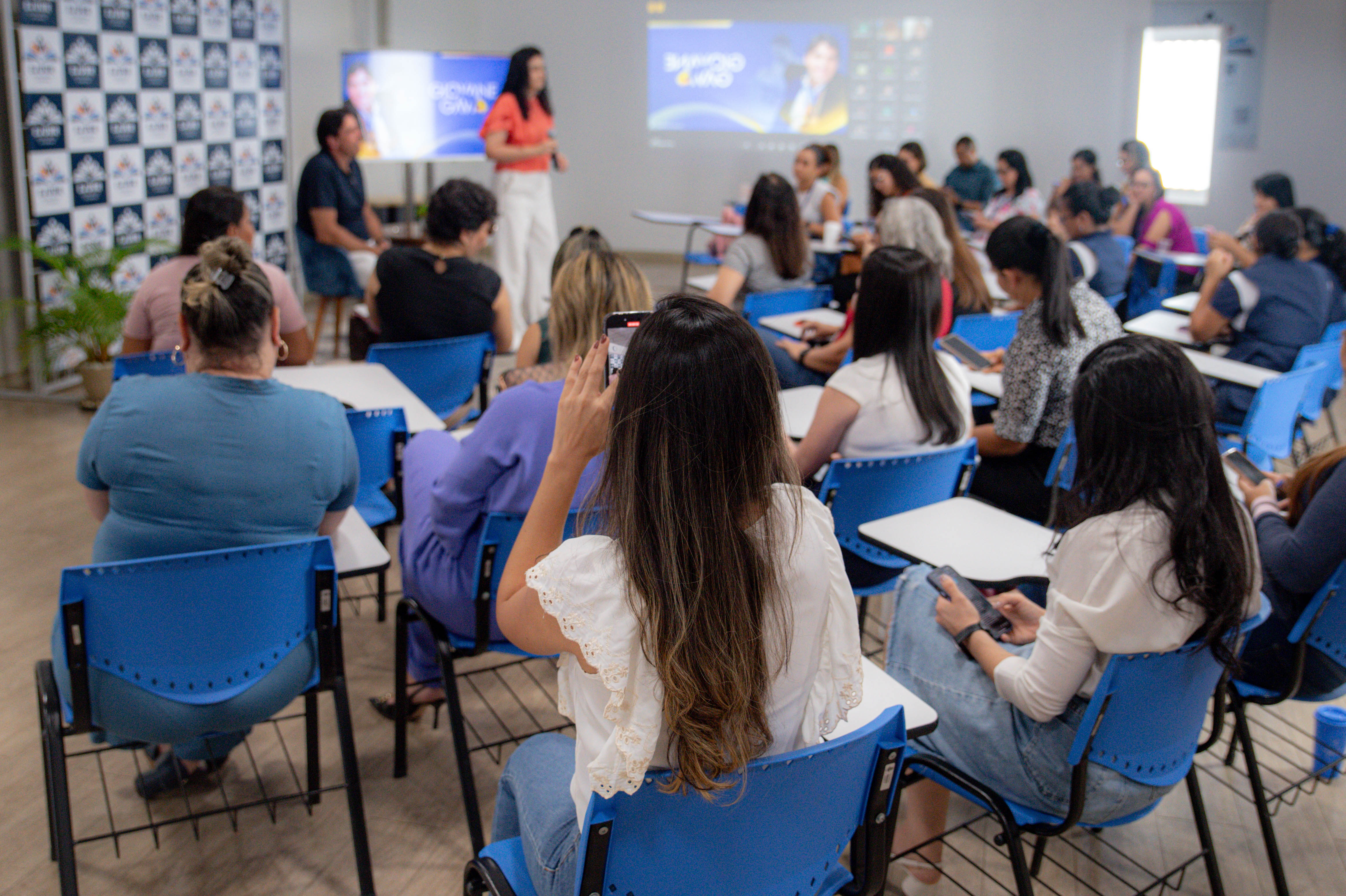 imagem colorida contem diversas pessoas em sala de aula na Escola Judicial de Roraima durante palestra assistindo e interagindo. 