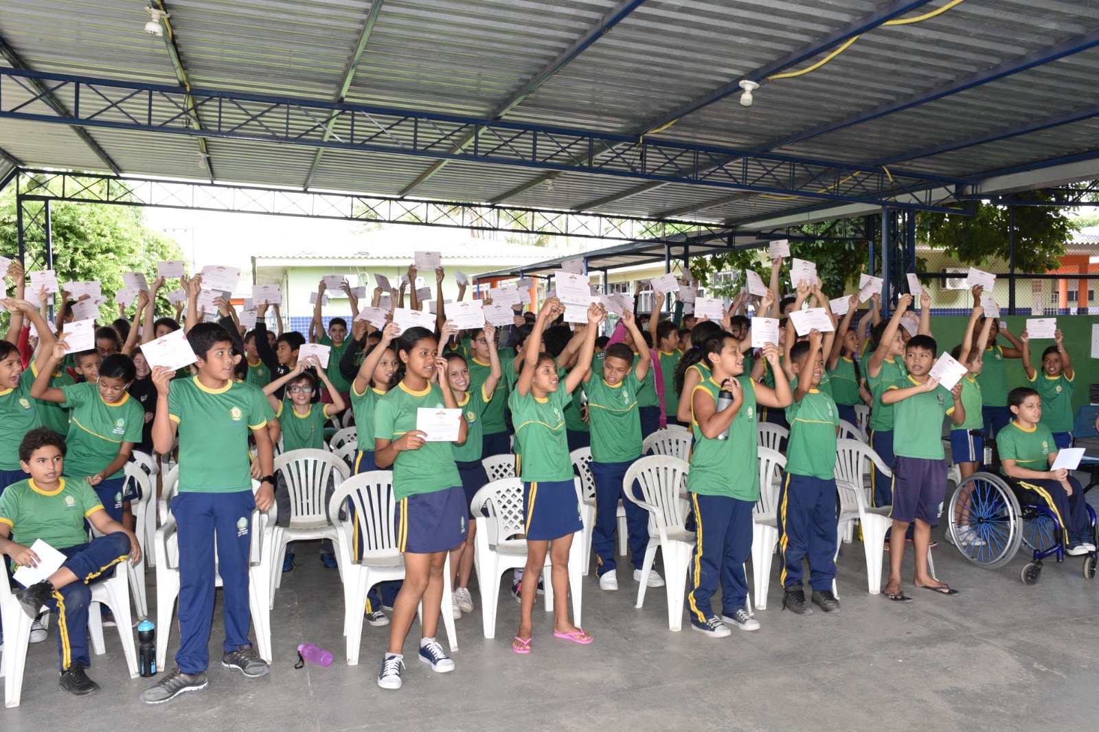 A imagem colorida mostra alunos do ensino fundamental em momento de dinâmica com papéis erguidos ao alto