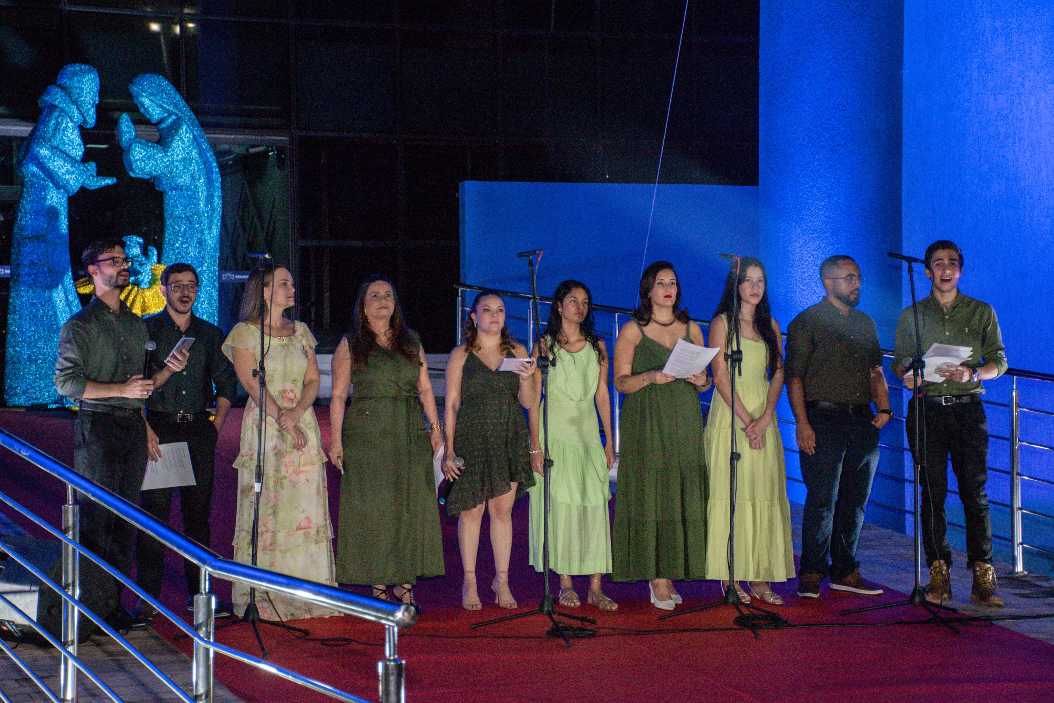 Imagem colorida mostra um coral musical contendo dez cantores se apresentando na entrada do  Palácio da Justiça Desembargador Robério Nunes dos Anjos, durante a cantata natalina do TJRR, sendo quatro homens e seis mulheres. 