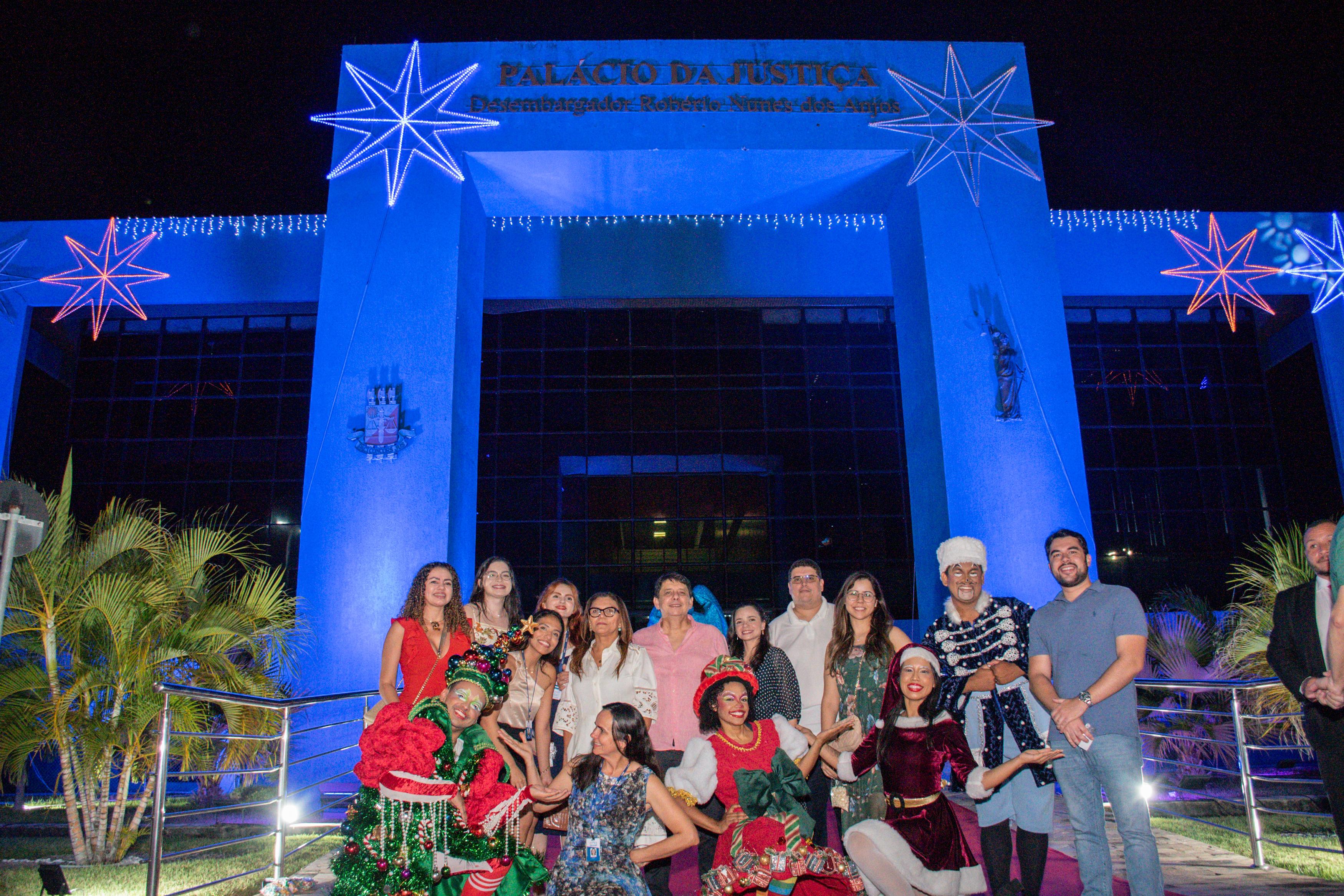  Imagem colorida mostra o presidente do TJRR, desembargador Jésus Nascimento, posando para fotografia ao lado da sua esposa, ao lado de mais nove servidores do TJRR, e mais quatro colaboradores do papai noel, em frente a entrada do  Palácio da Justiça Desembargador Robério Nunes dos Anjos,durante cantata natalina do TJRR.