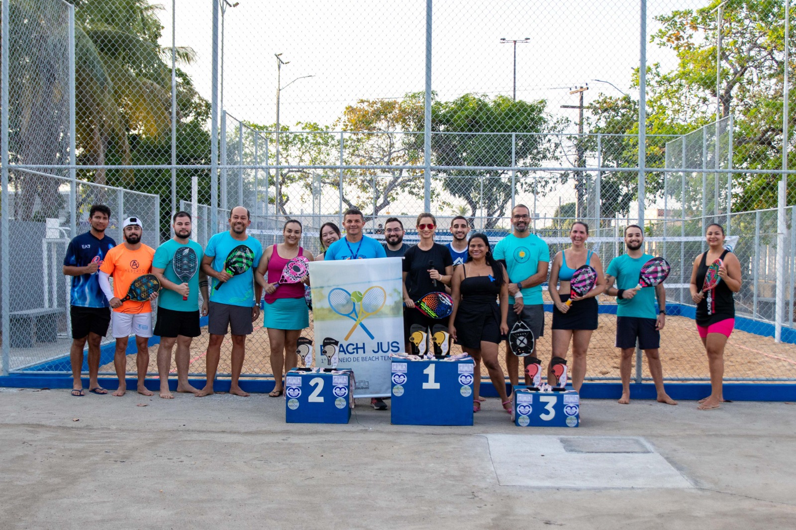 Foto colorida mostra todos os participantes do torneio posando para foto à frente de uma quadra do torenio.