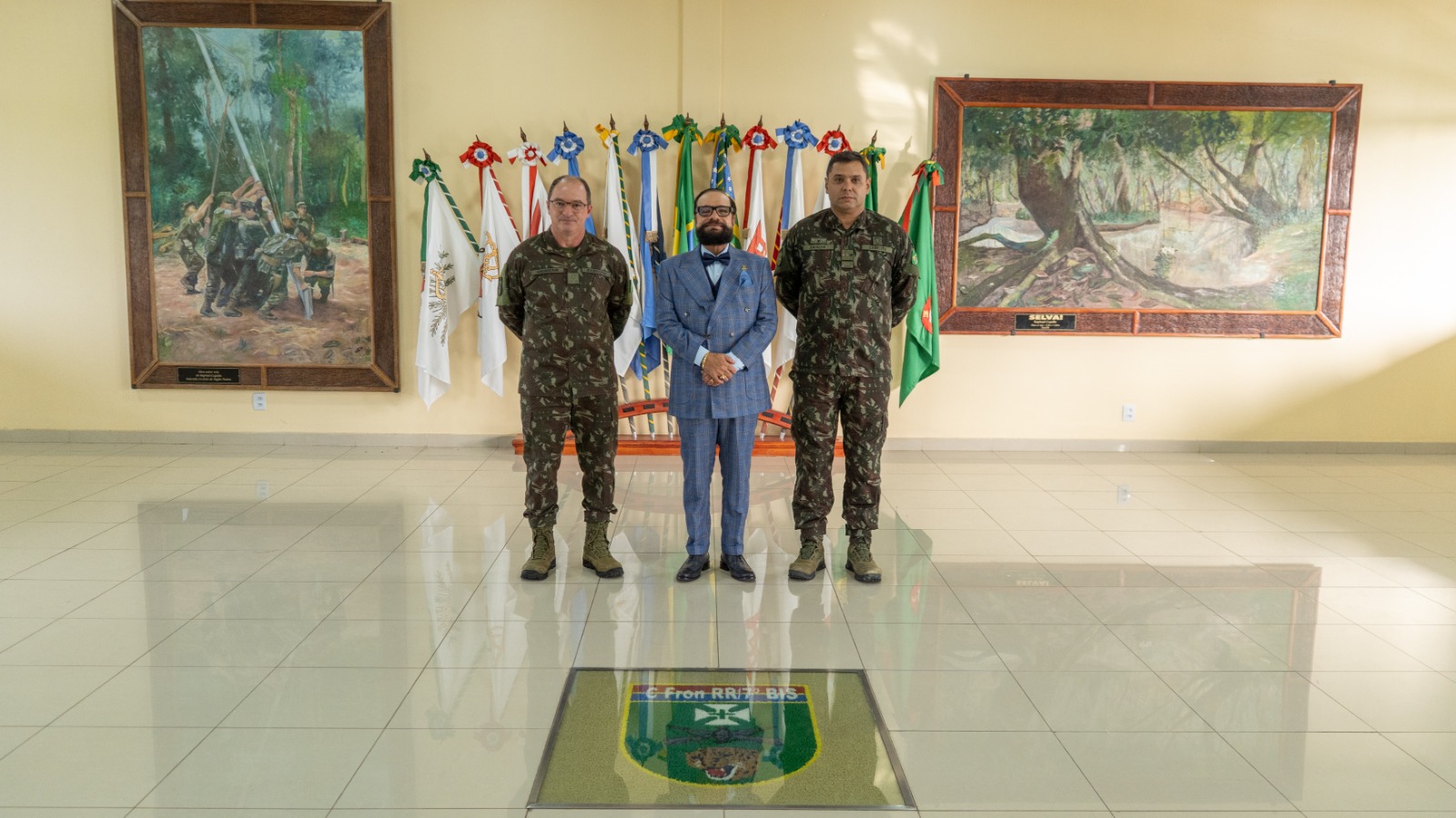 Presidente do TJRR, desembargador Leonardo Cupello ao lado de oficiais do Exército. Eles estão posando em um salão com bandeiras e obras de arte nas paredes