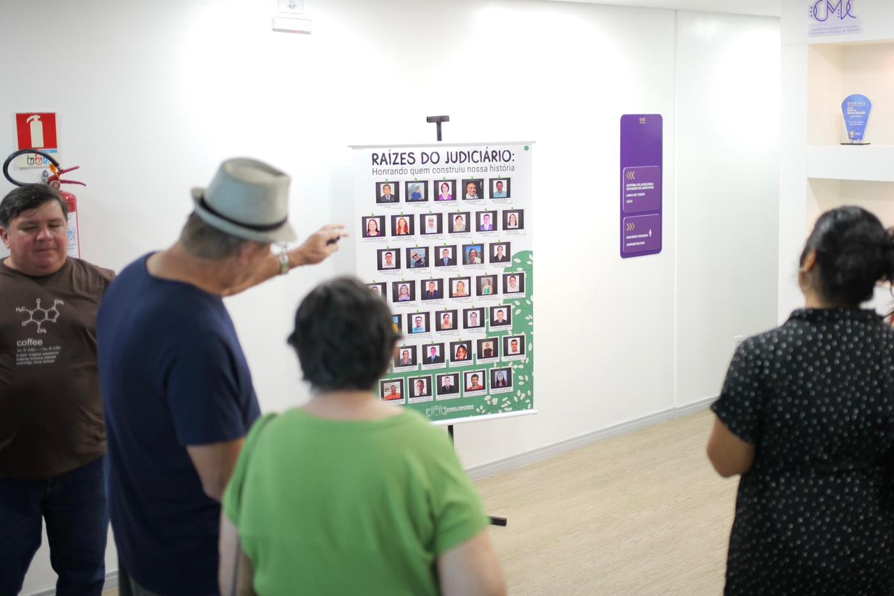 imagem colorida mostra quatro pessoas apreciando banner com fotografias de servidores e servidores do TJRR aposentados. imagem colorida mostra quatro pessoas apreciando banner com fotografias de servidores e servidores do TJRR aposentados.