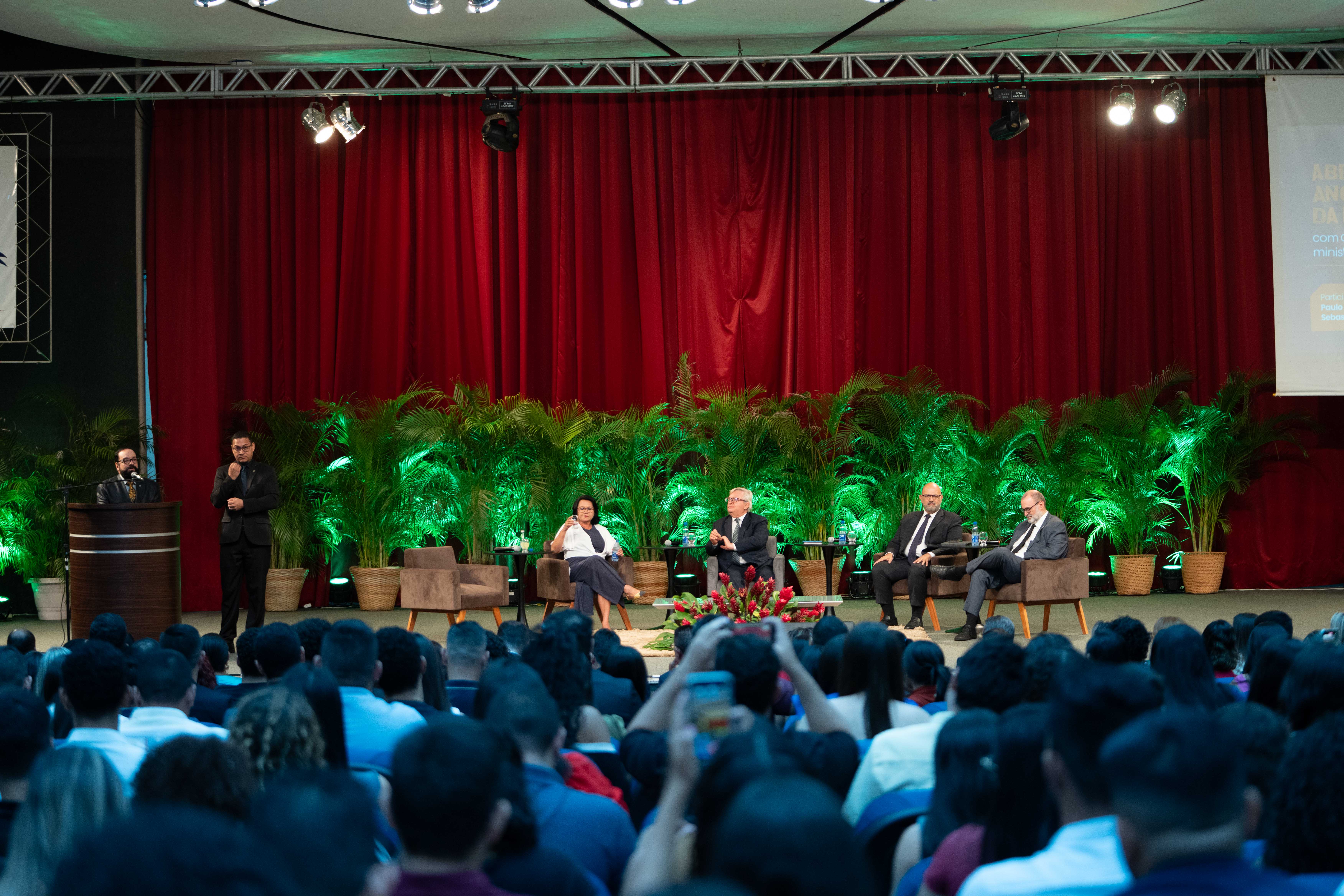 Foto colorida mostrando o Presidente do TJRR, Desembargador Leonardo Cupello discursando. Ao lado dele um interprete de libras. No centro do palco, estão a Desembargadora Tânia Vasconcellos, Diretora da Escola Judicial de Roraima e os ministros do STJ. 