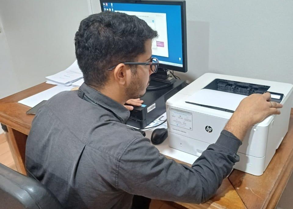 Imagem colorida mostrando um servidor da equipe do TJRR realizando ajustes técnicos em uma impressora Imagem colorida mostrando um servidor da equipe do TJRR realizando ajustes técnicos em uma impressora
