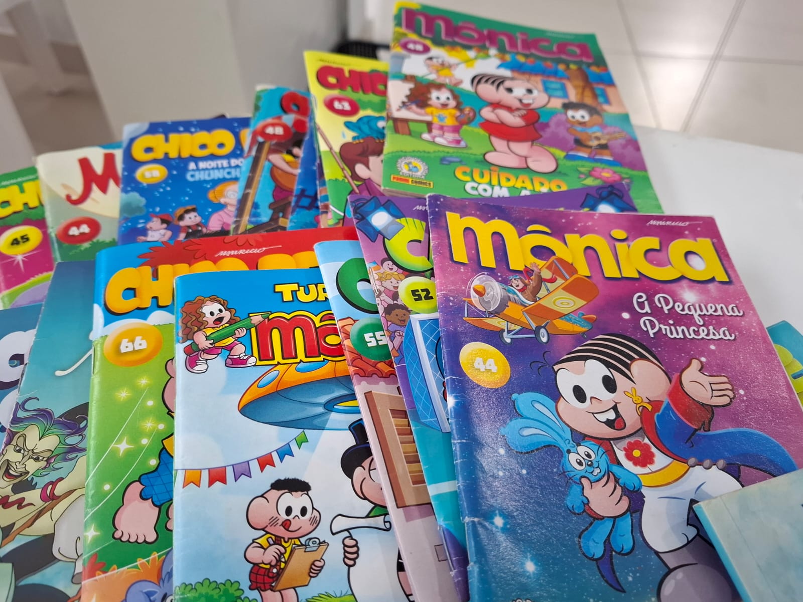 imagem colorida contém mesa com histórias em quadrinhos da “Turma da Mônica”. Um dos livros, à direita, aparece em destaque com o título “Mônica: a Pequena Princesa