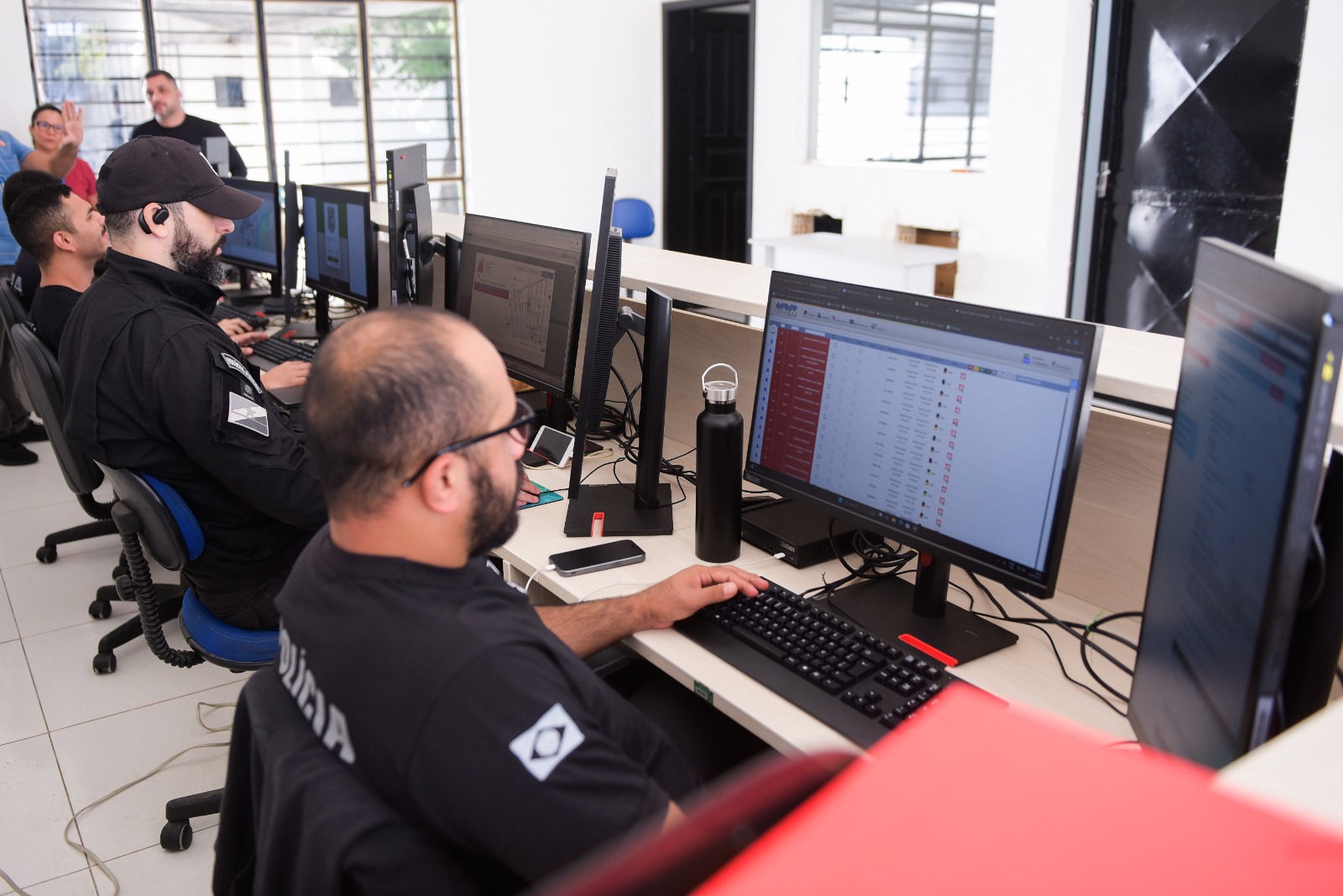  Imagem colorida mostra dois homens sentados em cadeiras de escritório em frente a computadores.