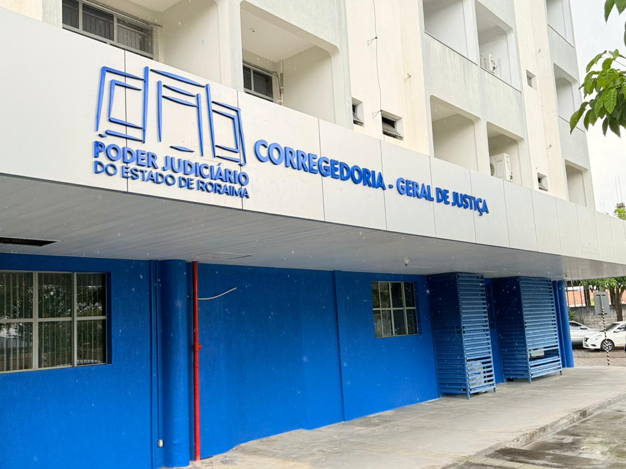 Imagem colorida da fachada de um prédio, mostrando a entrada da Corregedoria-Geral de Justiça do Poder Judiciário do Estado de Roraima. A parte inferior do edifício é pintada em um azul vibrante com as inscrições em relevo na marquise branca acima. Imagem colorida da fachada de um prédio, mostrando a entrada da Corregedoria-Geral de Justiça do Poder Judiciário do Estado de Roraima. A parte inferior do edifício é pintada em um azul vibrante com as inscrições em relevo na marquise branca acima.