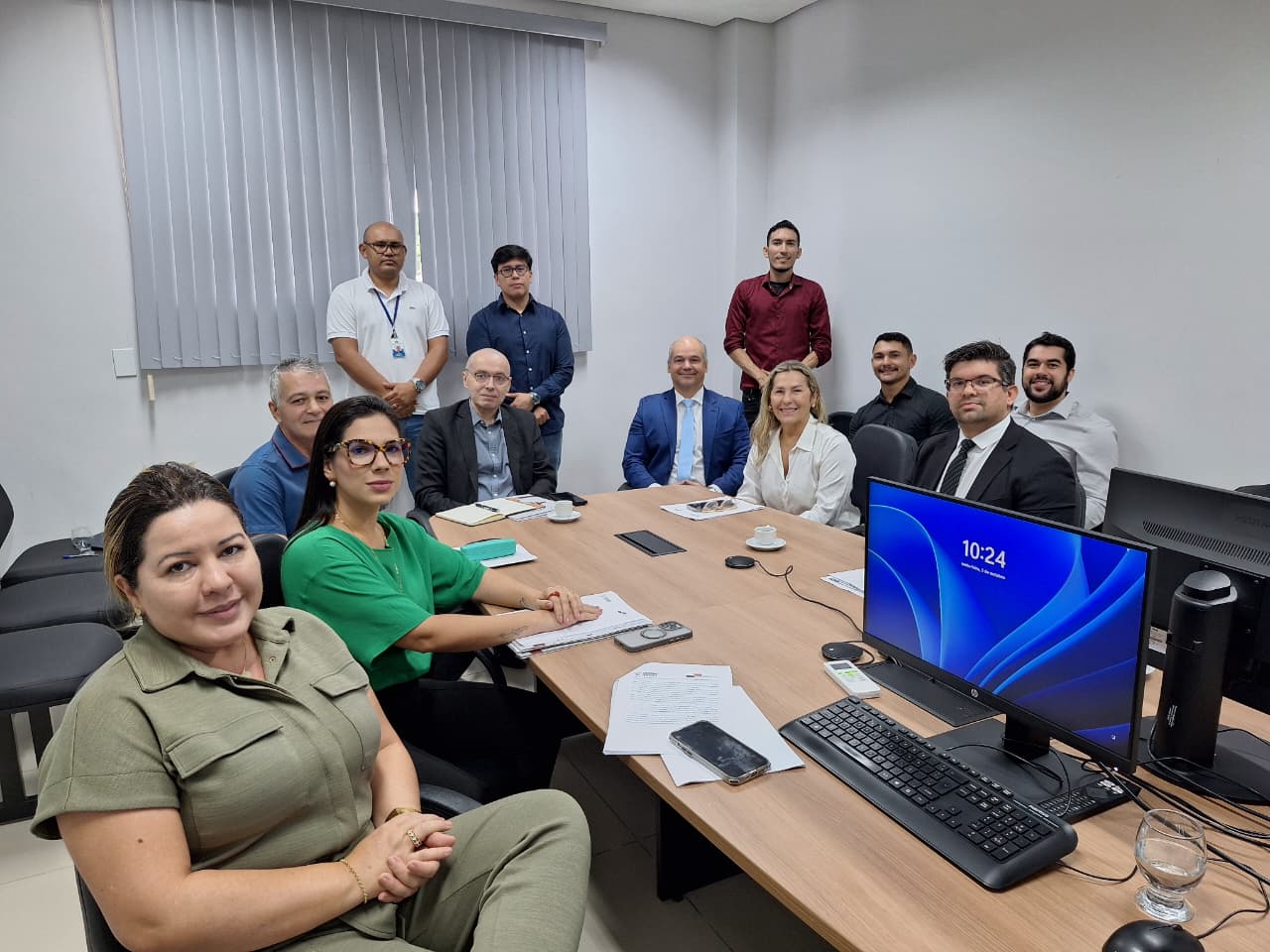 Foto colorida de uma reunião institucional em uma sala de escritório do Tribunal de Justiça de Roraima. Ao redor de uma mesa de madeira clara, estão 12 pessoas, entre homens e mulheres.