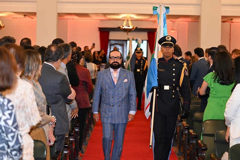 Foto colorida do presidente do TJRR, desembargador Leonardo Cupello, caminhando em um tapete vermelho, acompanhado por um militar que carrega uma bandeira, em cerimônia da abertura do evento com público dos dois lados.
