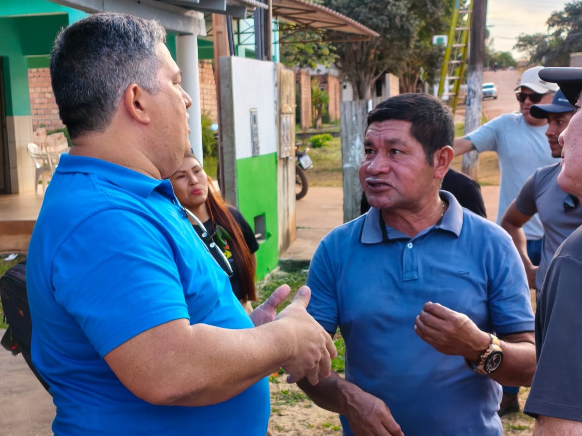 imagem colorida de um servidor da CGJ falando com seis pessoas, contendo uma mulher. O local mostra que é enfrente de uma casa.