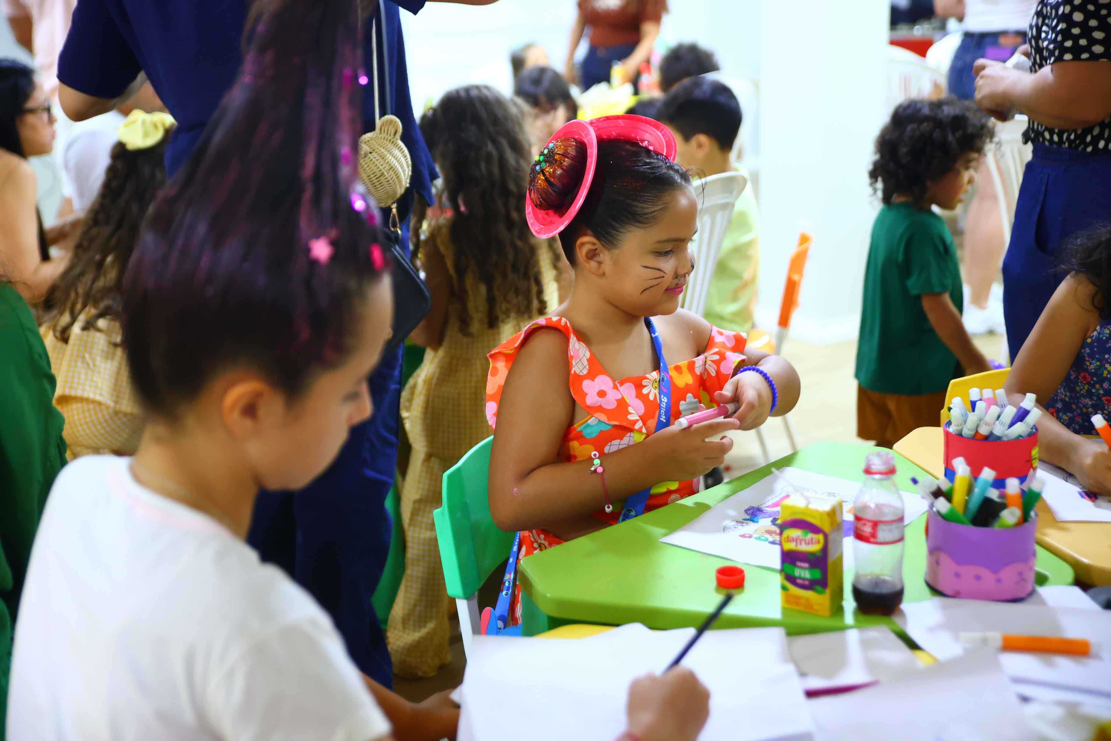 Imagem colorida dando enfoque em duas crianças pintando. Uma delas está com cabelo maluco fazendo referência há um prato de rosquinha. 