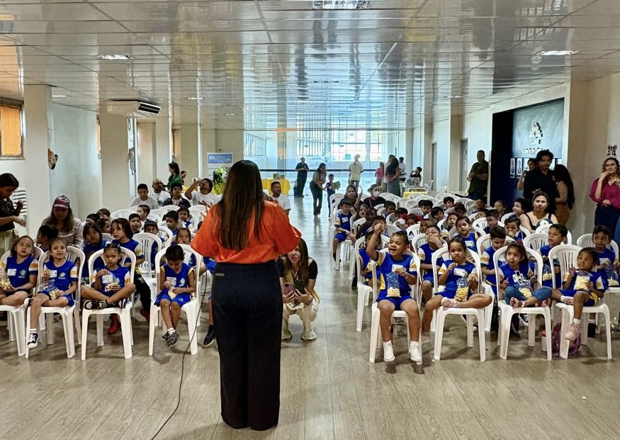 rianças uniformizadas assistindo atentas a apresentações em um salão. Uma cena mostra uma palestrante interagindo com a plateia; a outra, uma performance de um casal (um vestido de cozinheiro) no palco decorado com o logo do TJRR/EJURR. Crianças uniformizadas assistindo atentas a apresentações em um salão. Uma cena mostra uma palestrante interagindo com a plateia; a outra, uma performance de um casal (um vestido de cozinheiro) no palco decorado com o logo do TJRR/EJURR.