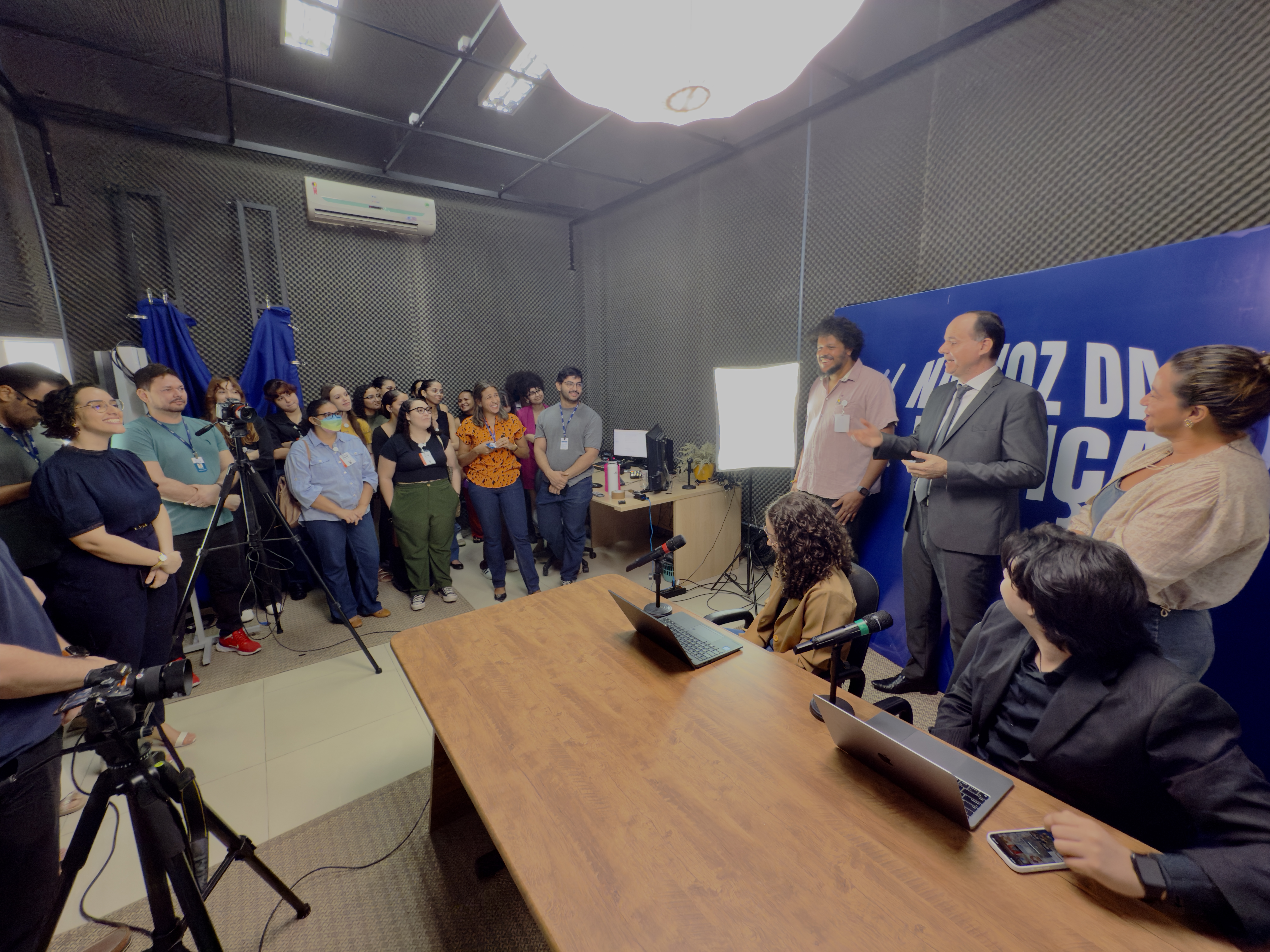 Imagem colorida mostra um estúdio de gravação com um grupo de pessoas em uma visita. O desembargador Cristóvão Suter, de terno cinza, está em pé à direita, conversando com um grupo. Há duas pessoas sentadas em frente a uma mesa com notebooks. Imagem colorida mostra um estúdio de gravação com um grupo de pessoas em uma visita. O desembargador Cristóvão Suter, de terno cinza, está em pé à direita, conversando com um grupo. Há duas pessoas sentadas em frente a uma mesa com notebooks.