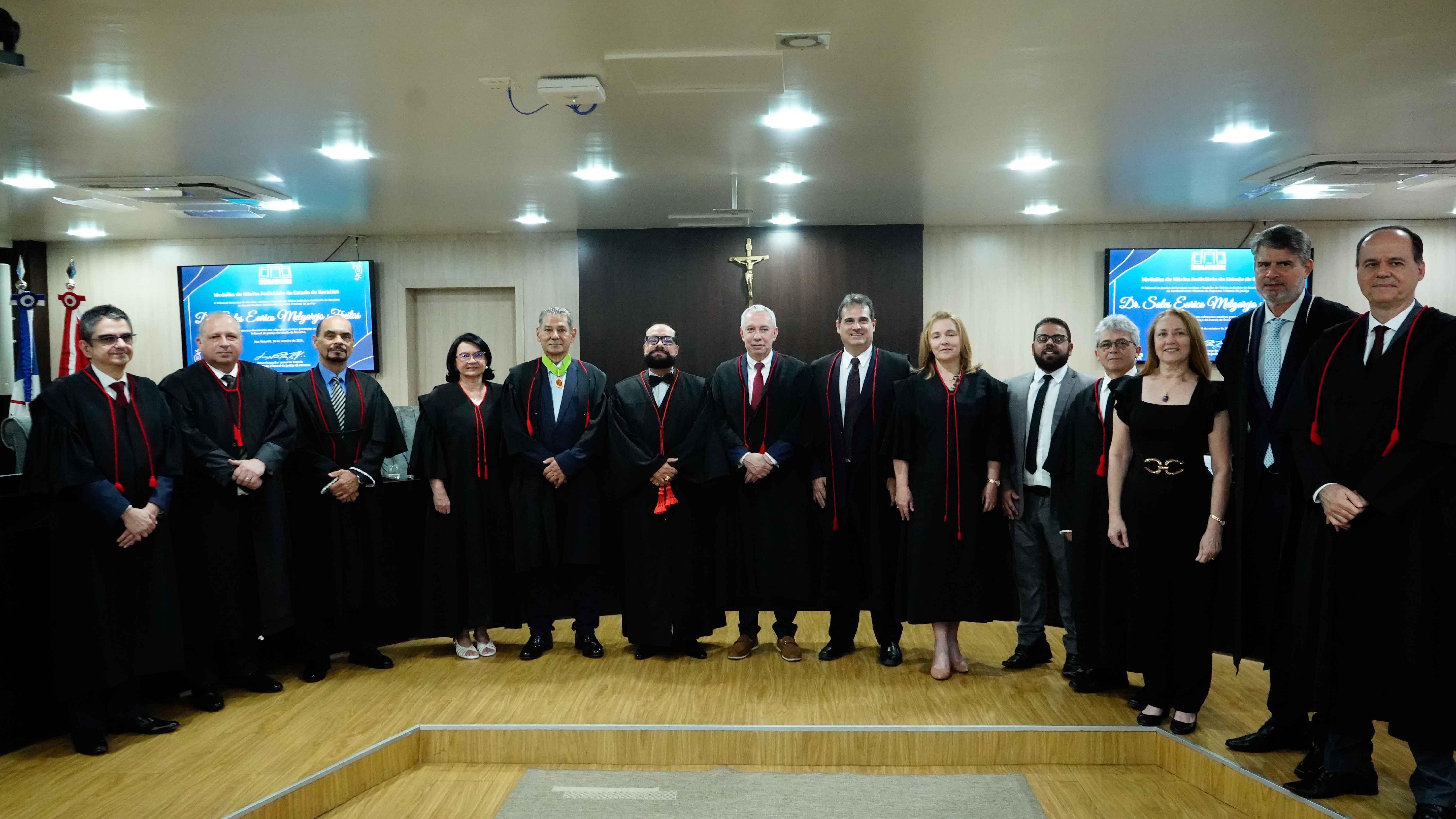 Imagem colorida mostra grupo de autoridades posa para foto oficial em um plenário. O Desembargador Leonardo Cupello e o Procurador Sales Eurico Melgarejo Freitas, usando a comenda, estão entre os presentes, a maioria vestindo togas pretas e alinhados em frente à bancada de madeira. Imagem colorida mostra grupo de autoridades posa para foto oficial em um plenário. O Desembargador Leonardo Cupello e o Procurador Sales Eurico Melgarejo Freitas, usando a comenda, estão entre os presentes, a maioria vestindo togas pretas e alinhados em frente à bancada de madeira.