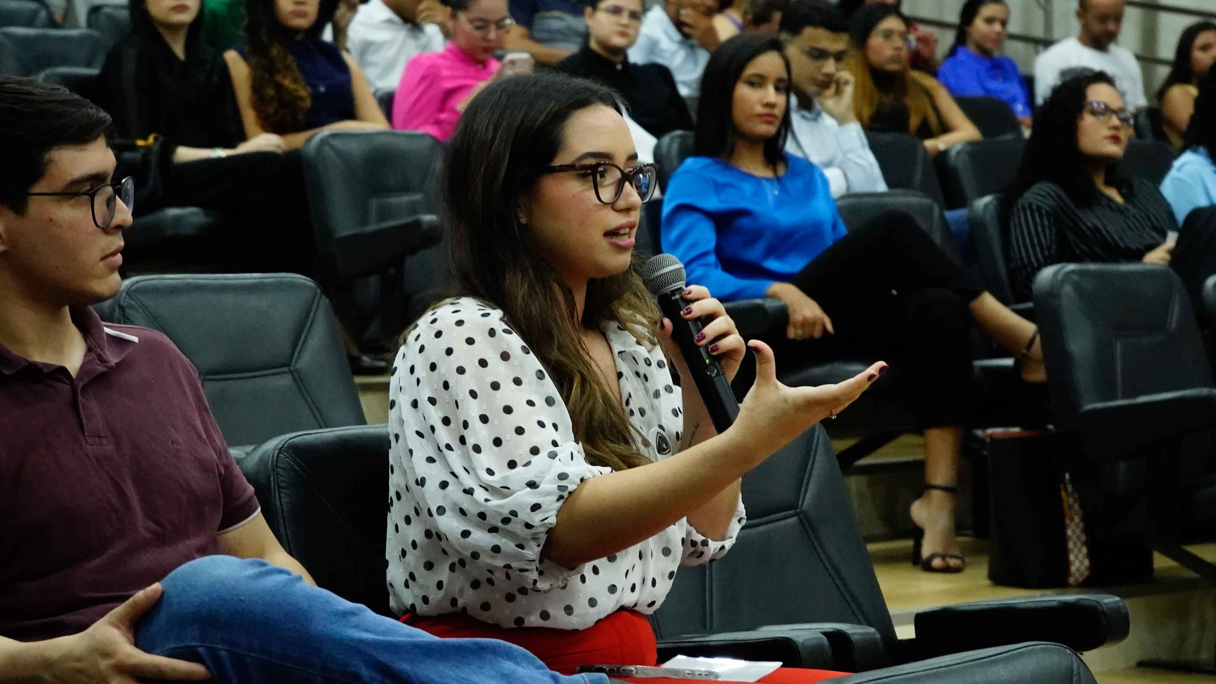imagem colorida de uma academica na plateia fazendo uma pergunta
