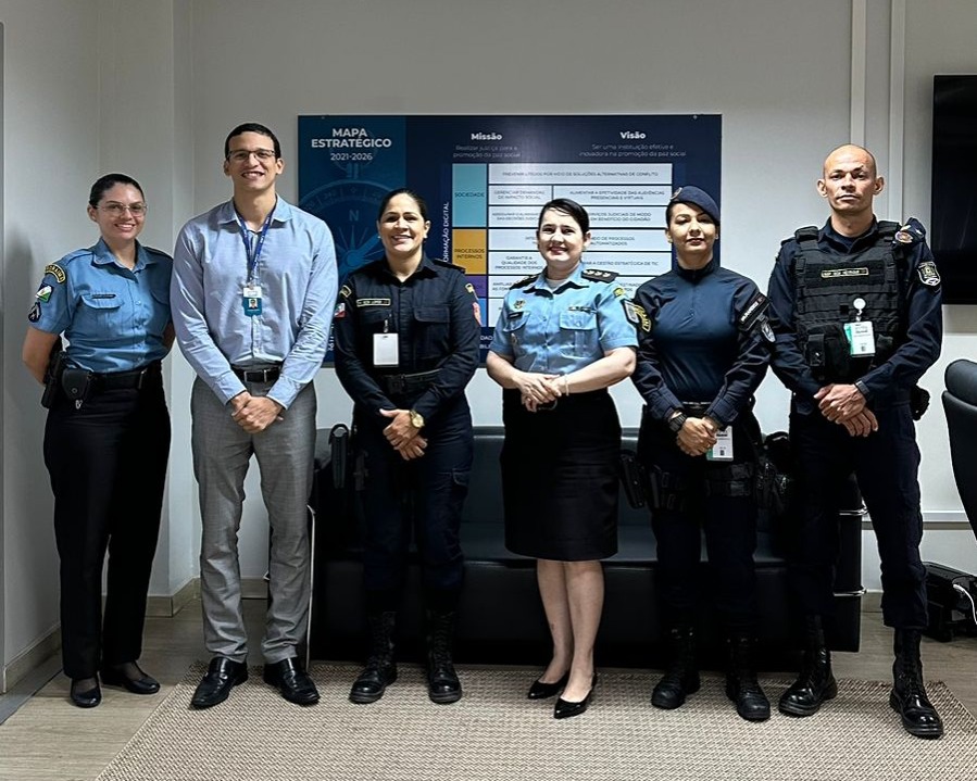 Foto colorida mostra seis pessoas em pé posando para foto. Entre eles, o secretário Geral do TJRR, Henrique Tavares, e guardas municipais