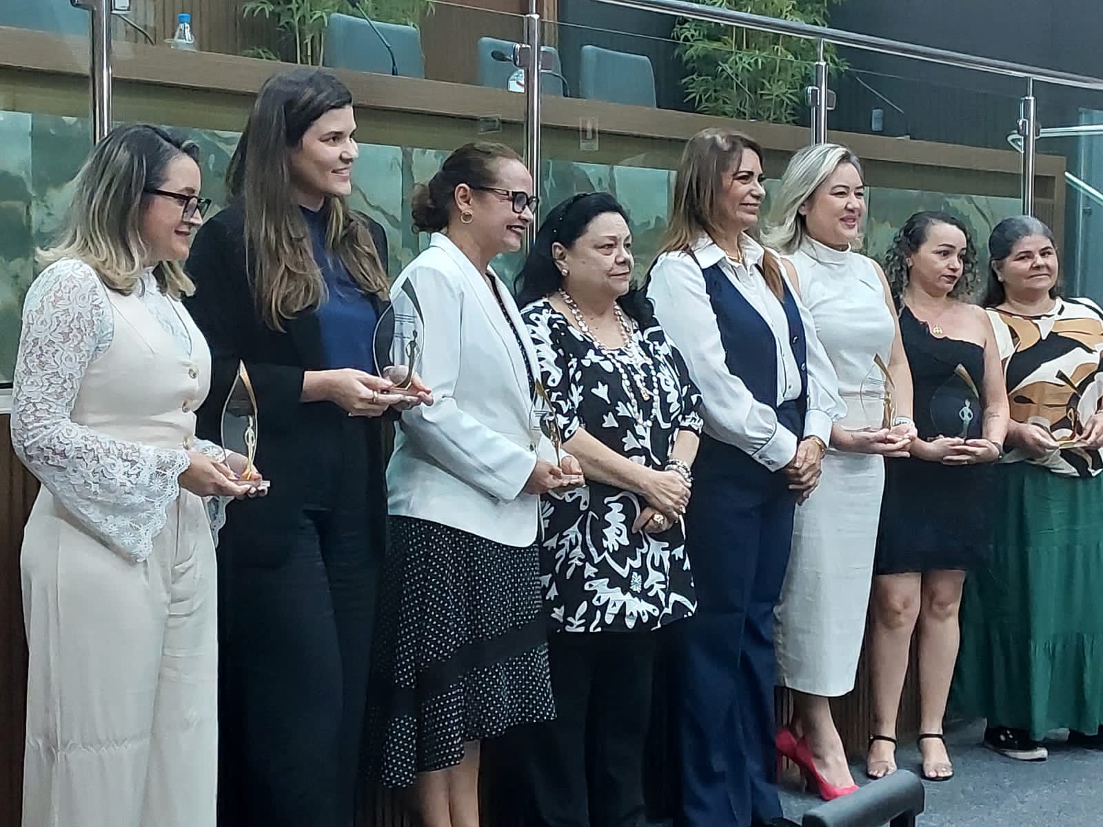  Imagem colorida de oito mulheres reunidas com troféus posando para uma foto. 