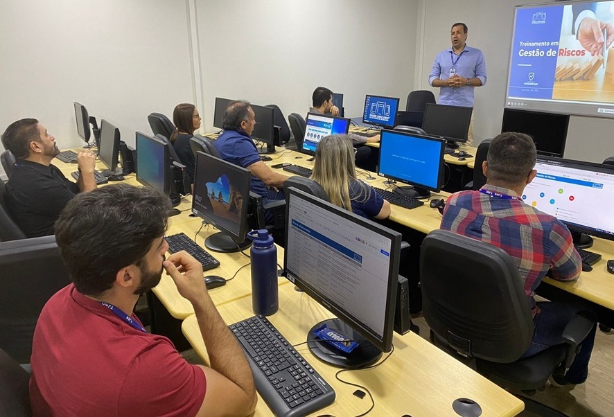 foto colorida de uma sala com computadores enfileirados ocupados por servidores. Ministrando a aula é um servidor do TJRR