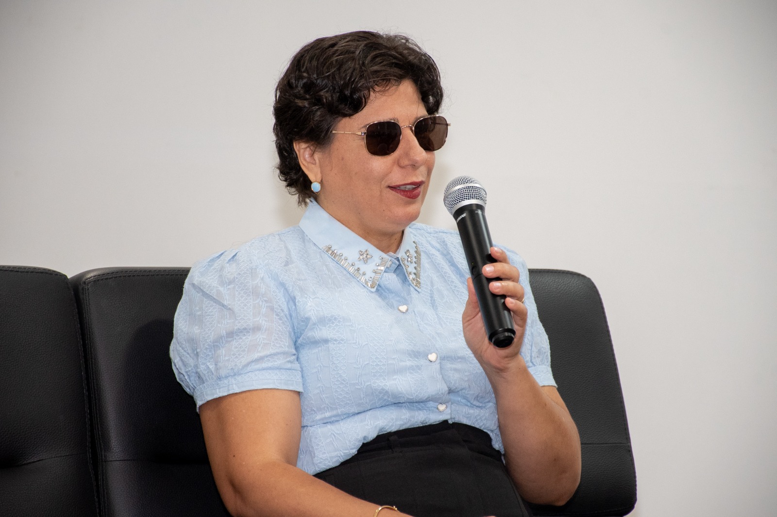 Foto colorida mostra a integrante da Comissão de Acessibilidade e Inclusão, Vera Lúcia Sábio, falando ao microfone durante a roda de conversa.