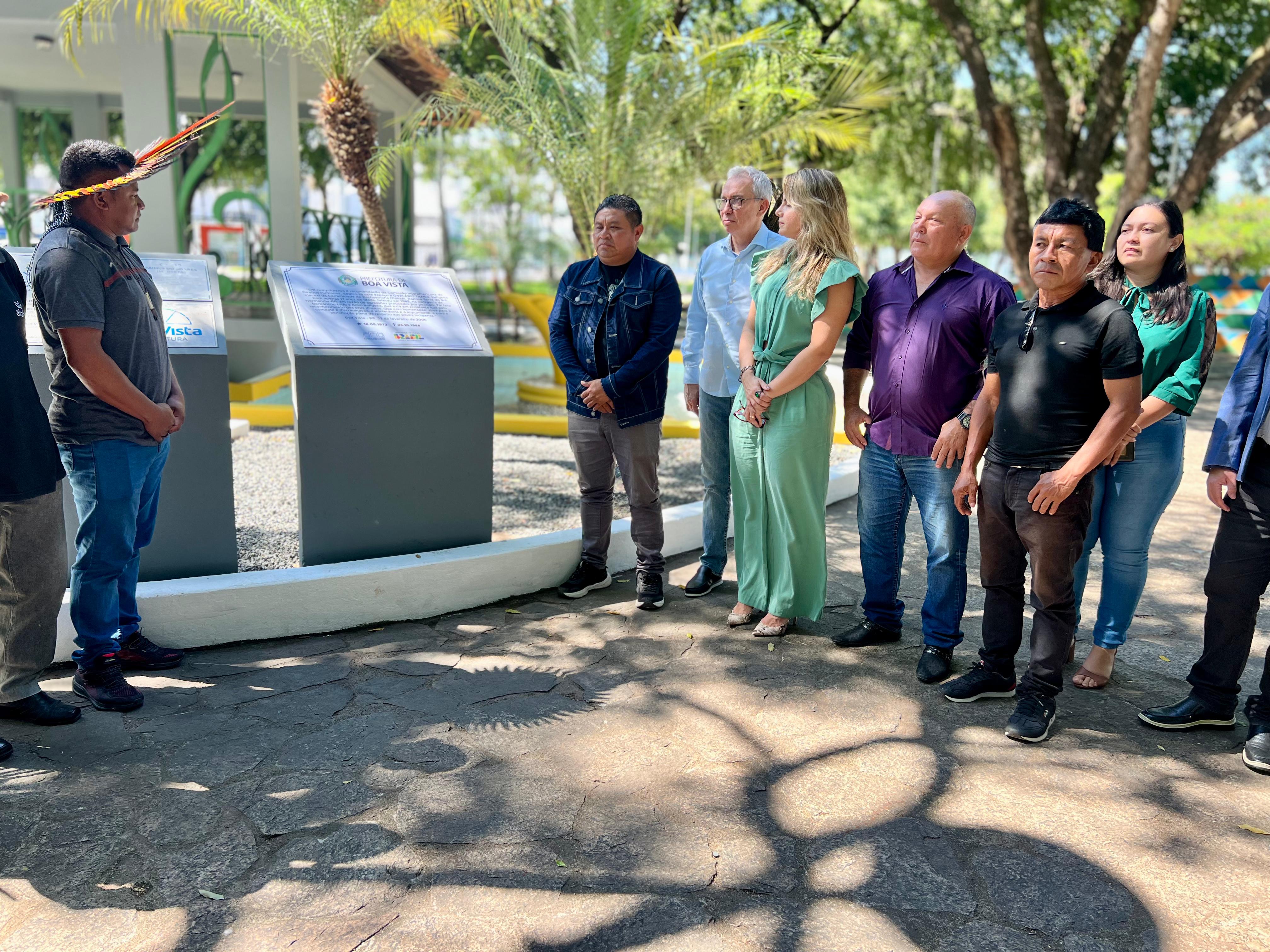 Imagem colorida mostra o desembargador Almiro Padilha, juntamente com autoridades convidadas na praça do coreto, ao lado da placa revitalizada do memorial do indígena Ovelário Tames.Abaixo a frase “Homenagem aos Povos Originários - Memorial Indígena revitalizado no Dia dos Direitos Humanos reforça luta por Justiça em Roraima.”