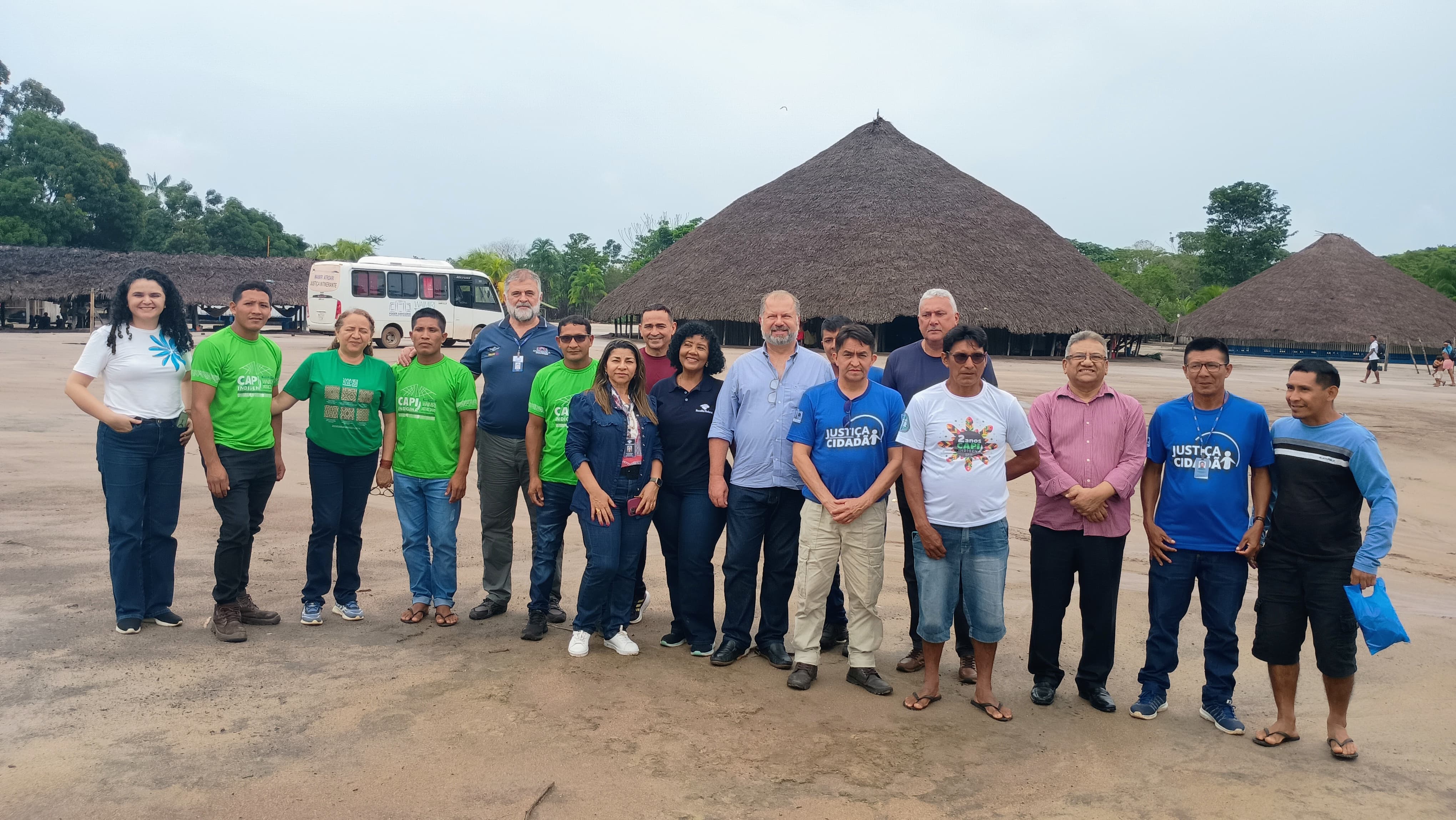 Imagem colorida mostra servidores da Ouvidoria-Geral do Tribunal de Justiça de Roraima e representantes da Terra Indígena Waimiri-Atroari posando para foto em área externa da comunidade Indígena Waimiri-Atroari, entre eles se destacam o servidor da Ouvidoria-Geral do Tribunal de Justiça de Roraima, Amadeu Triani, além da representante da representante da Escola Judicial de Roraima, Tatiana Saldanha. Abaixo a frase “CIDADANIA - Ouvidora do TJRR  realiza atendimento aos povos originários da T.I. Waimiri-Atroari”.