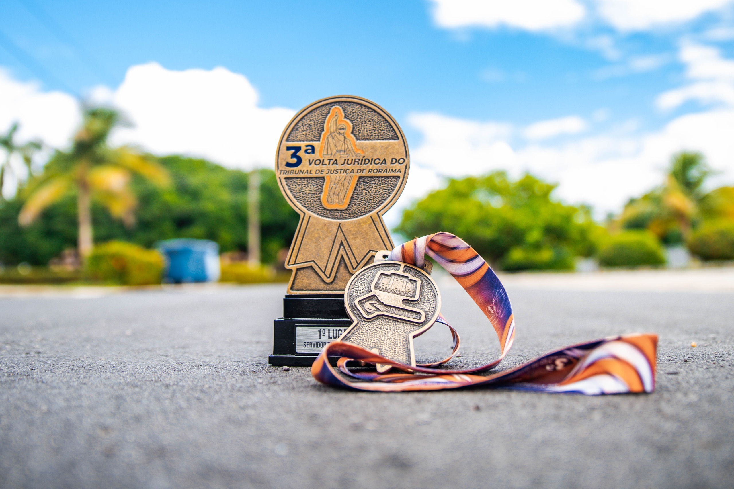 foto colorida mostra a medalha e o troféu da 3ª edição da corrida "Volta jurídica”, do Tribunal de Justiça de Roraima.