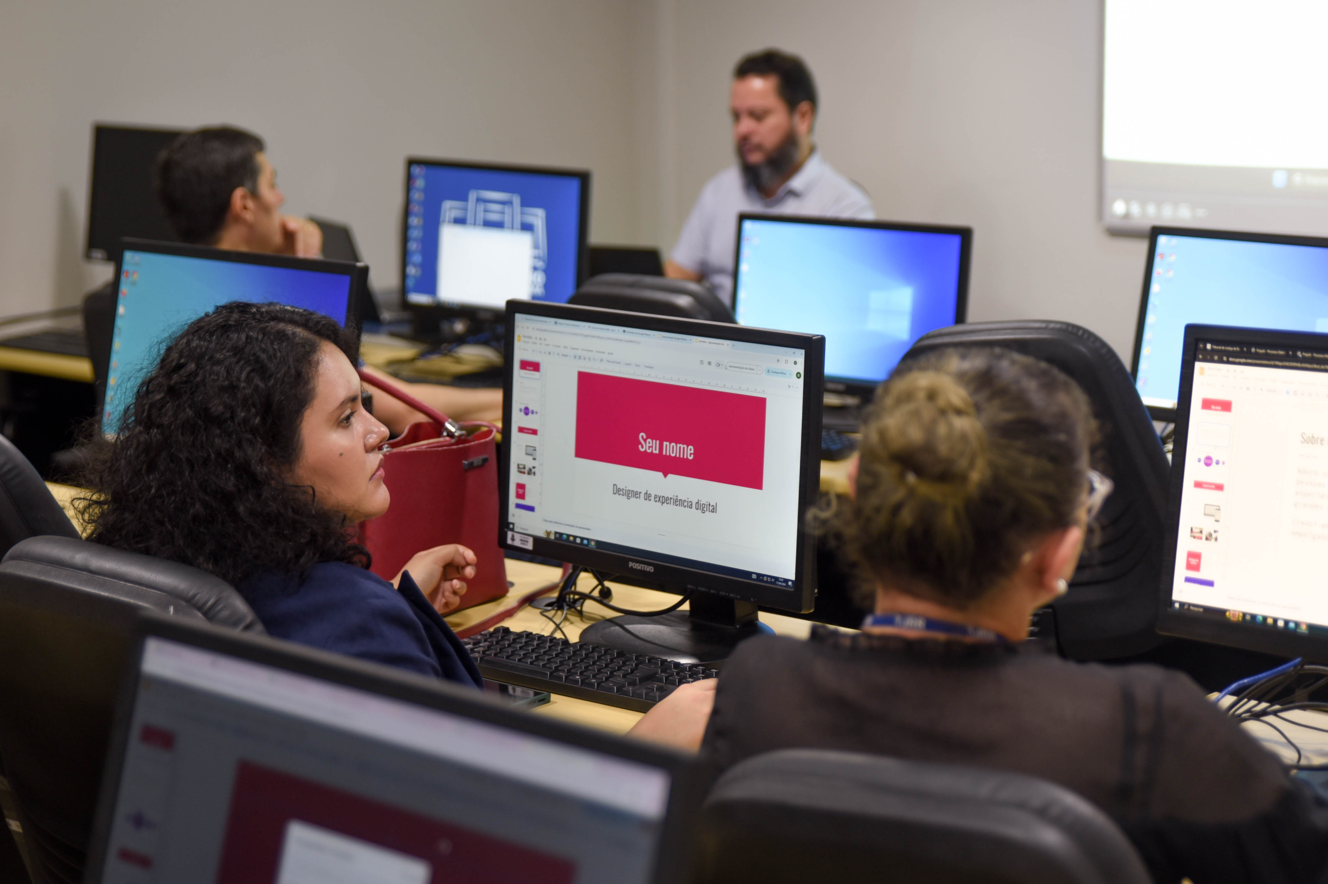 Imagem colorida mostrando pessoas sentadas em frente a computadores