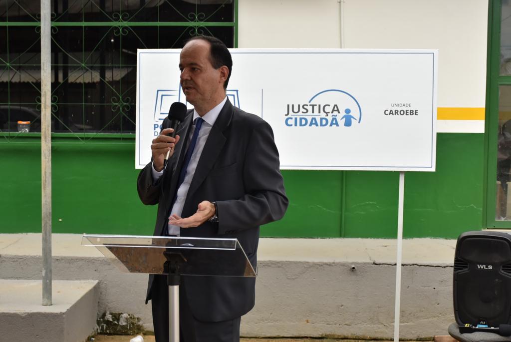 Foto colorida mostra o presidente, desembargador Cristóvão Súter, falando no microfone, logo atrás dele a placa da polo do Justiça Cidadã de Caroebe. 