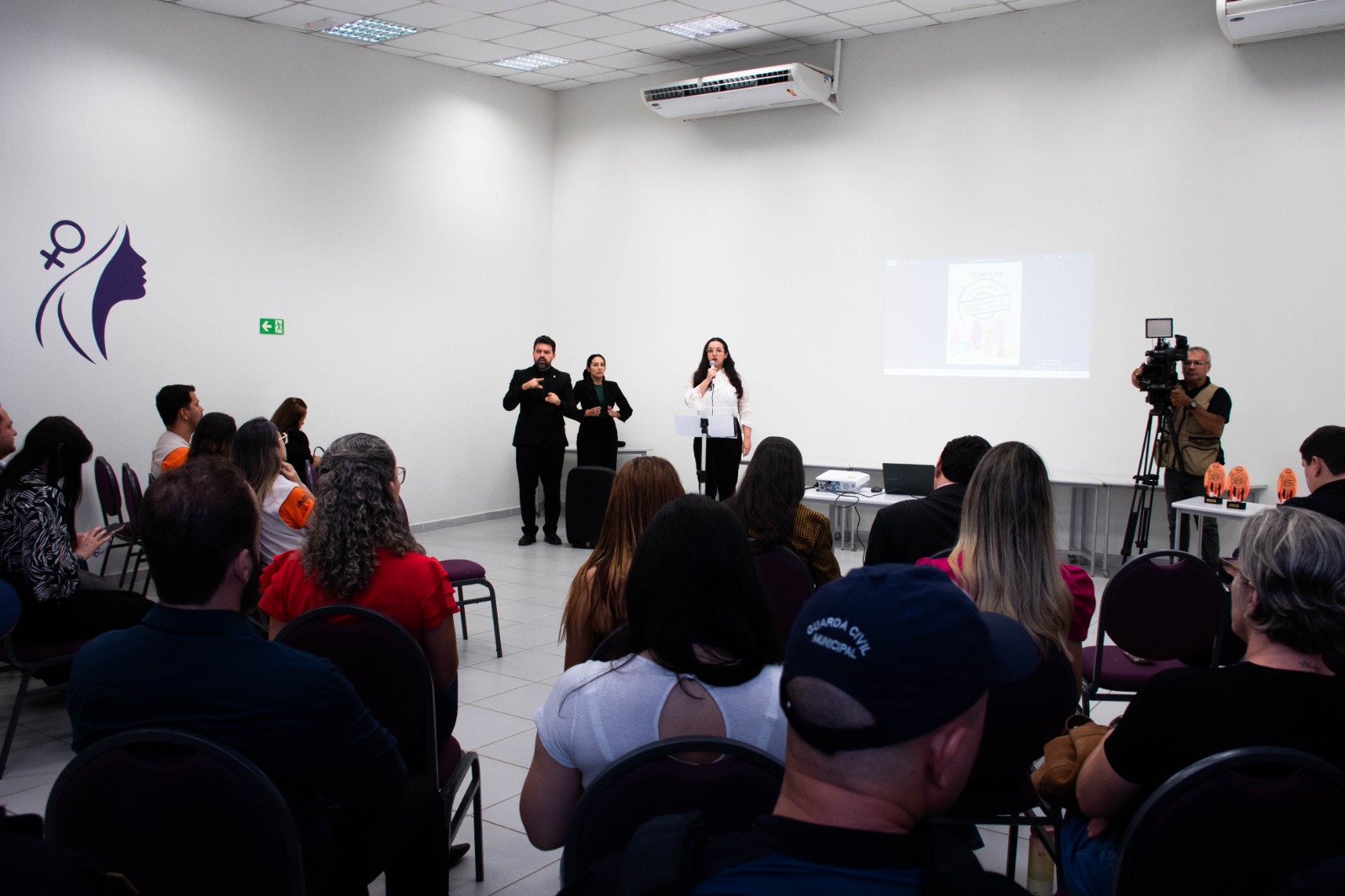 Foto colorida mostra uma plateia de costas assistindo a fala da juiza Suelen Alves